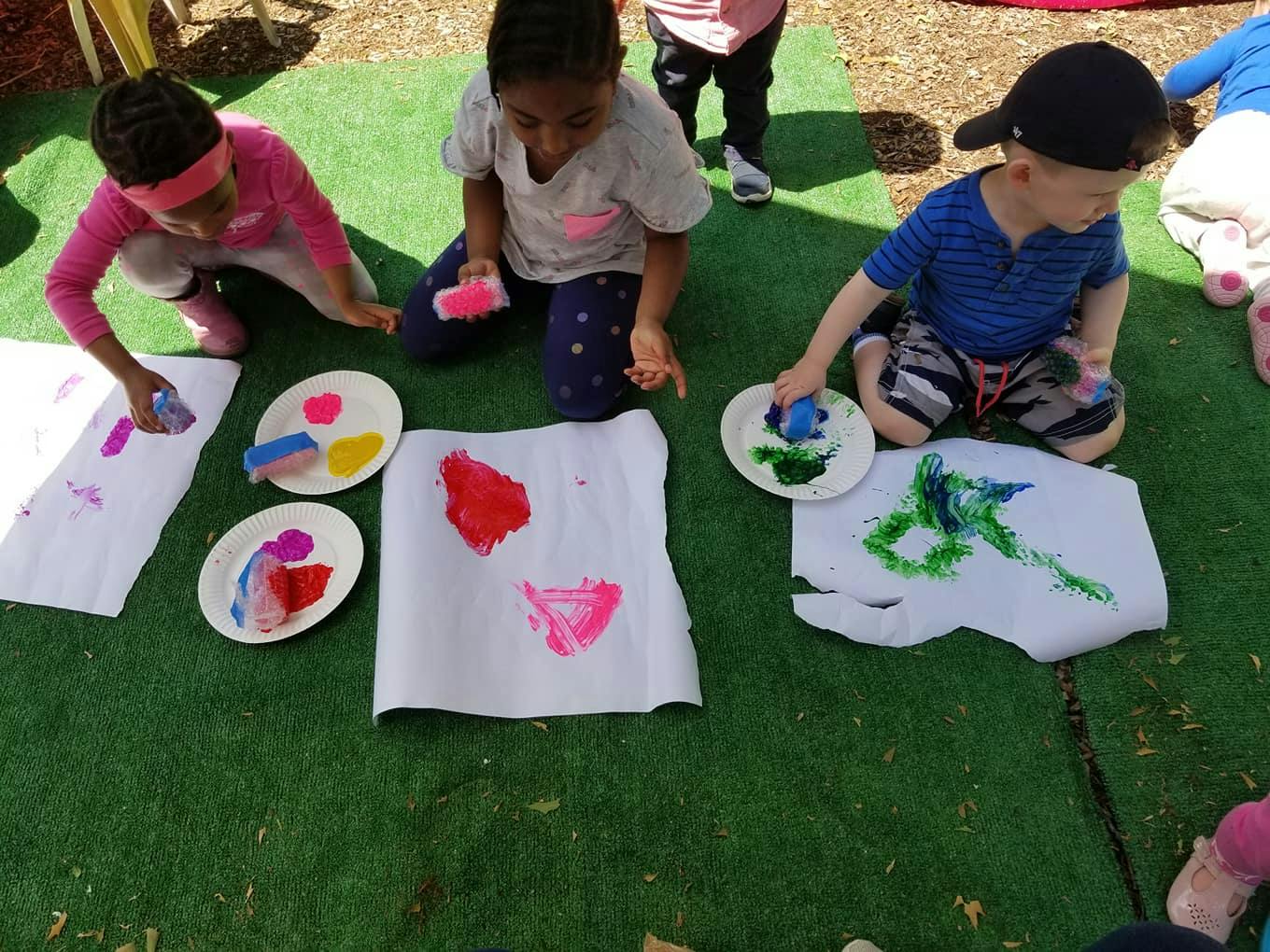 Three children painting on paper on the ground