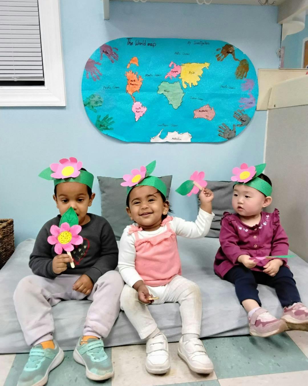 Three children wearing flower headbands sitting on a mat