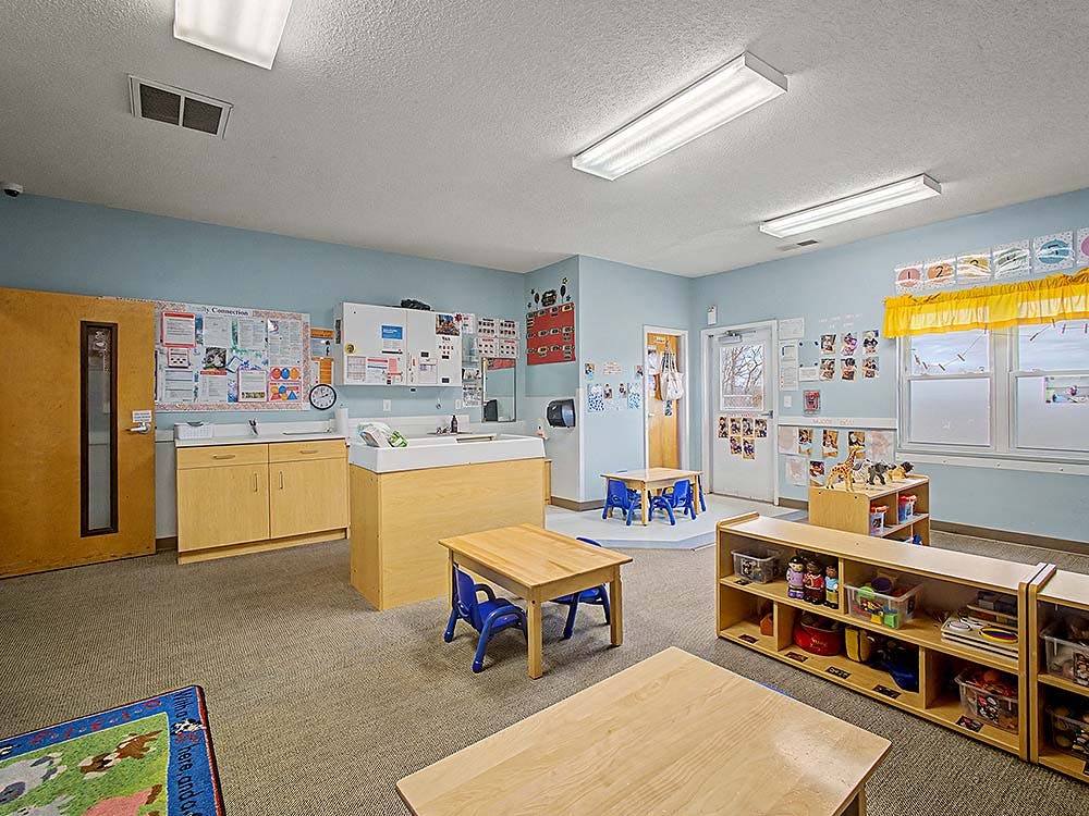 Classroom with small tables and chairs, shelves with toys, and a diaper changing station