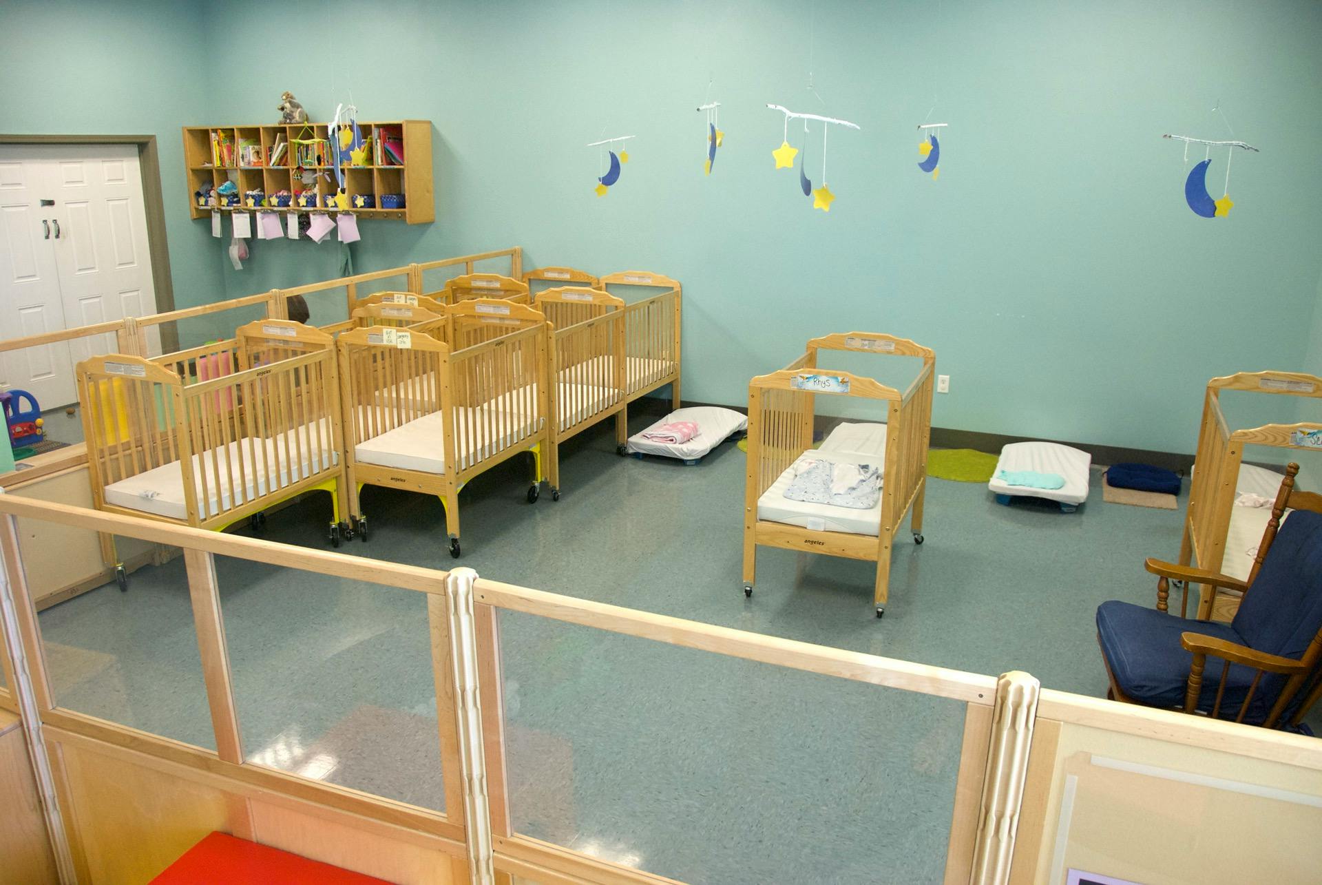 Nursery room with multiple cribs and a bookshelf