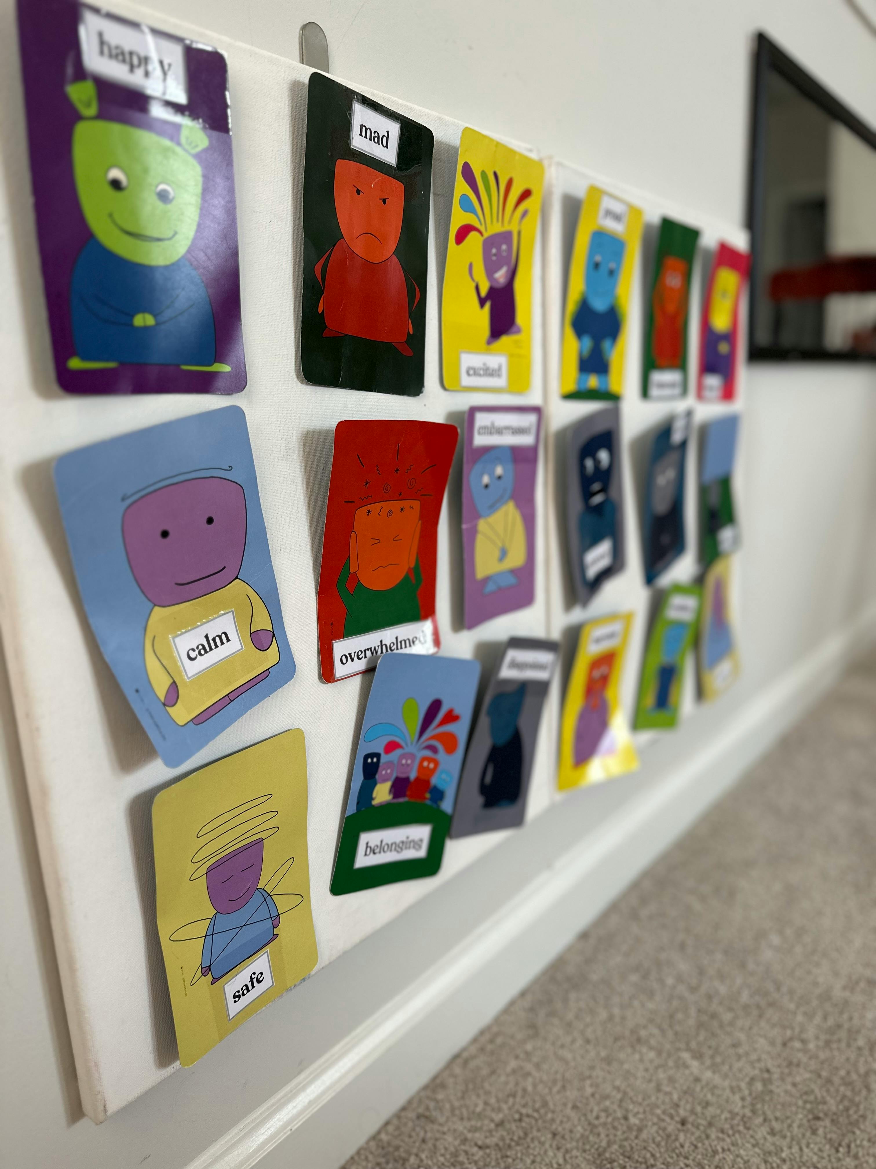 Multiple colorful cards with cartoon figures and emotion words displayed on a wall