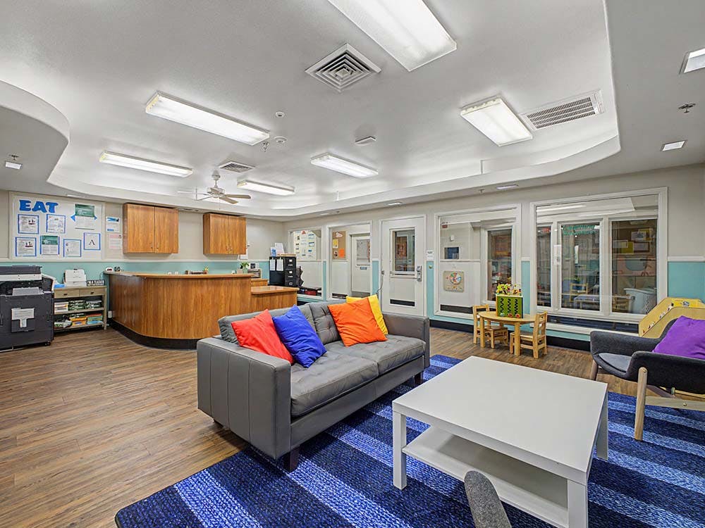 Lobby with a gray couch, blue rug, wooden reception desk, and glass windows
