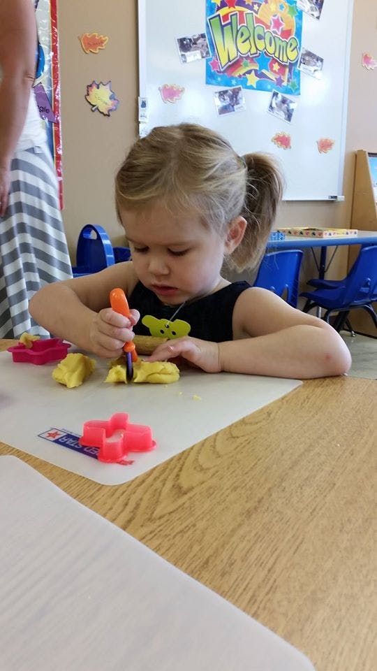 Child playing with yellow playdough and cutters at a table