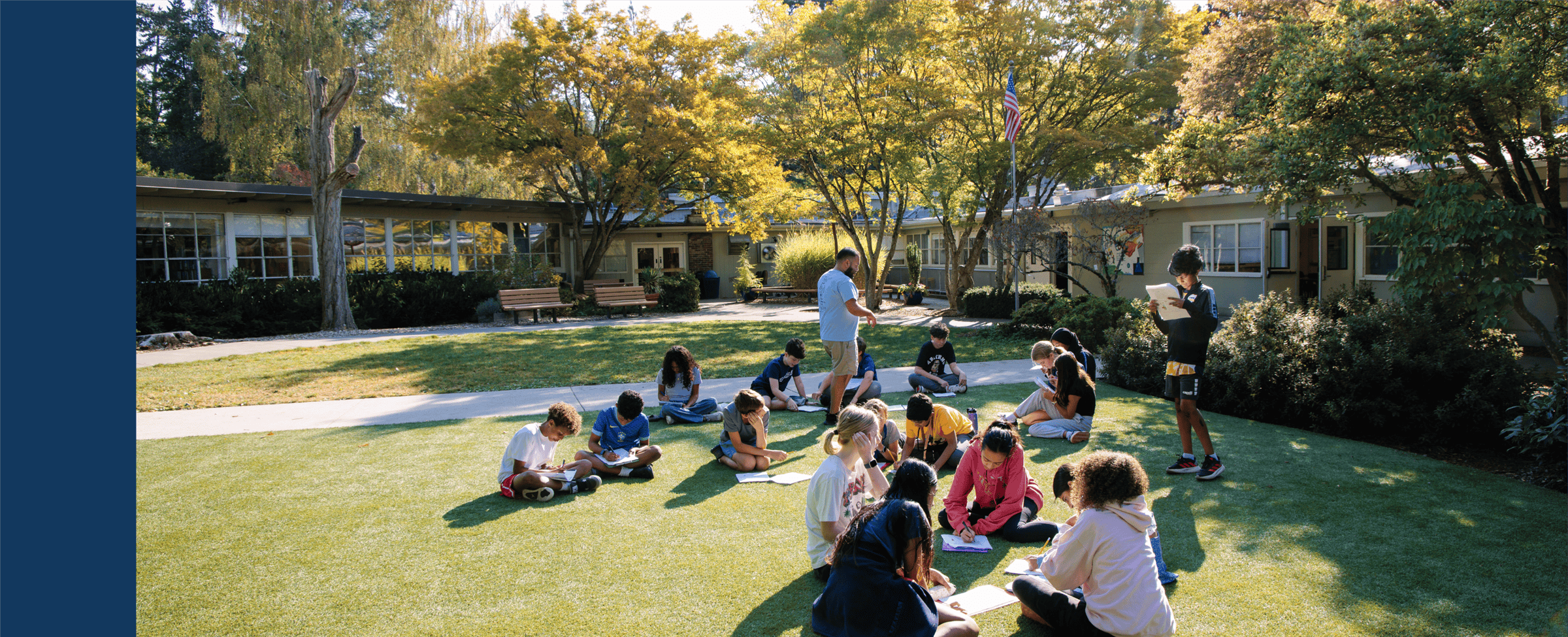 Teacher and students sitting on the grass outside with notebooks