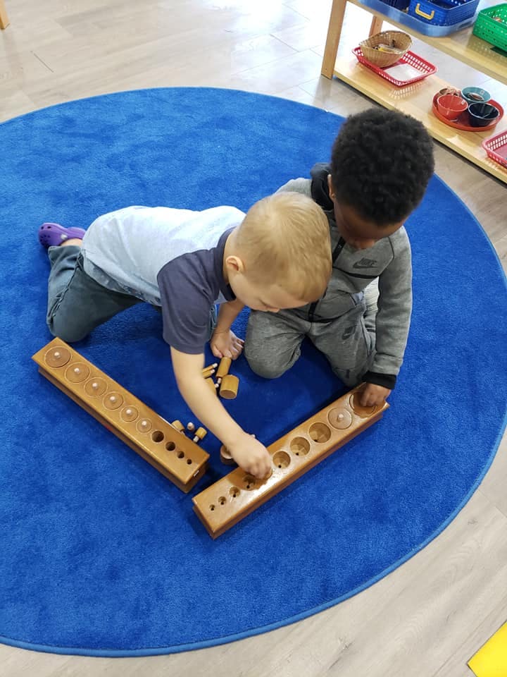 Two children playing with wooden peg boards on a blue rug