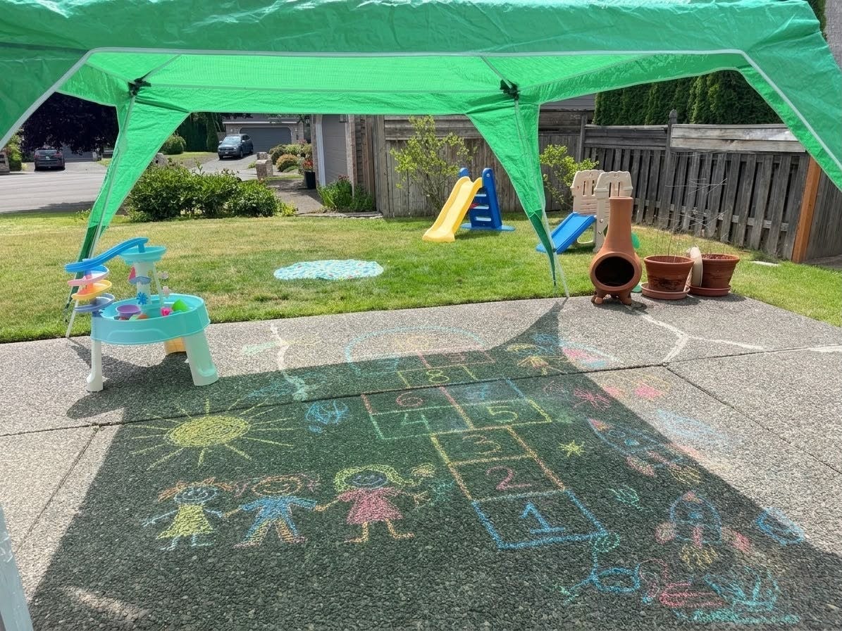 Chalk drawings of hopscotch and figures on a driveway under a green canopy