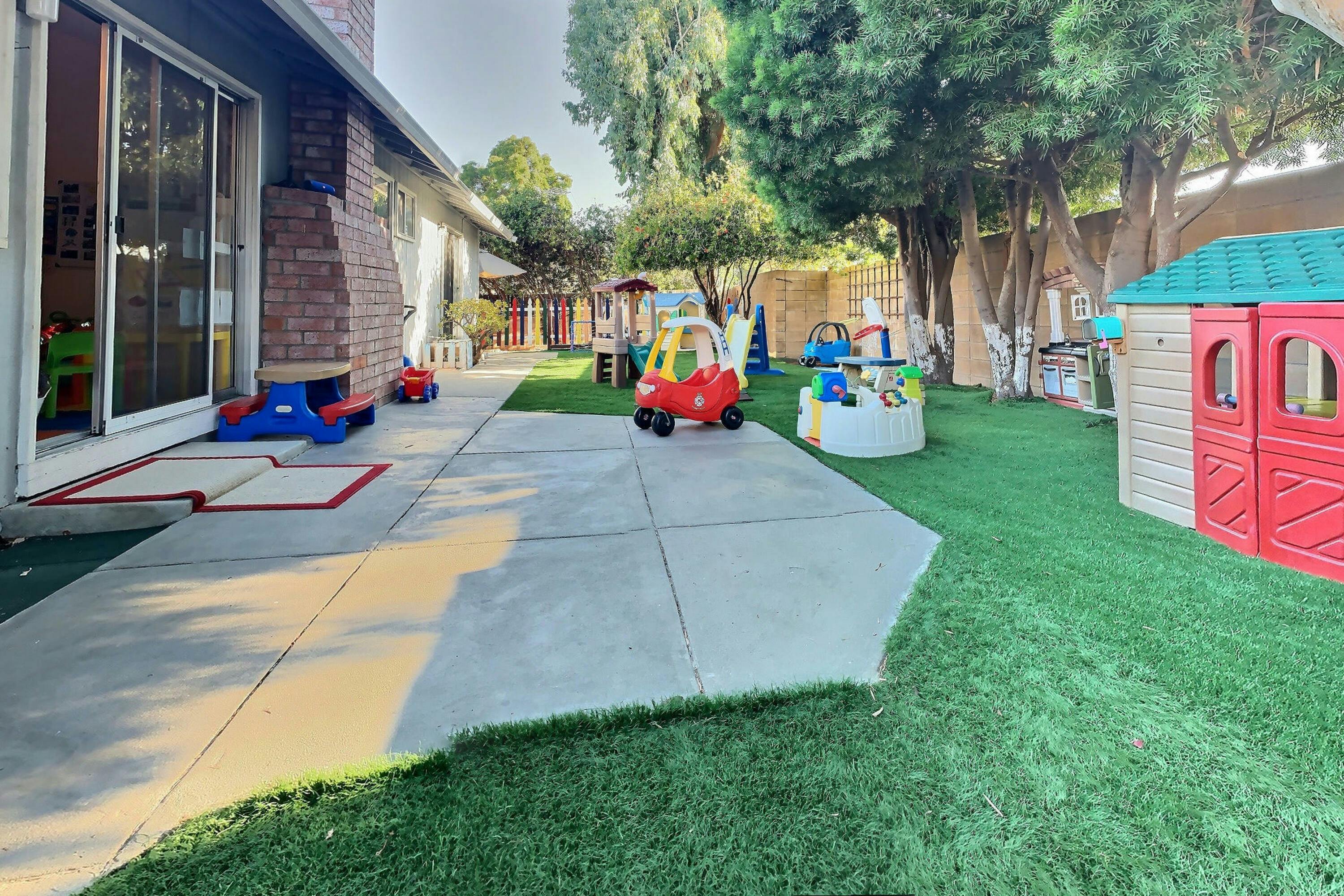 Outdoor play area with artificial turf, concrete path, and playhouses