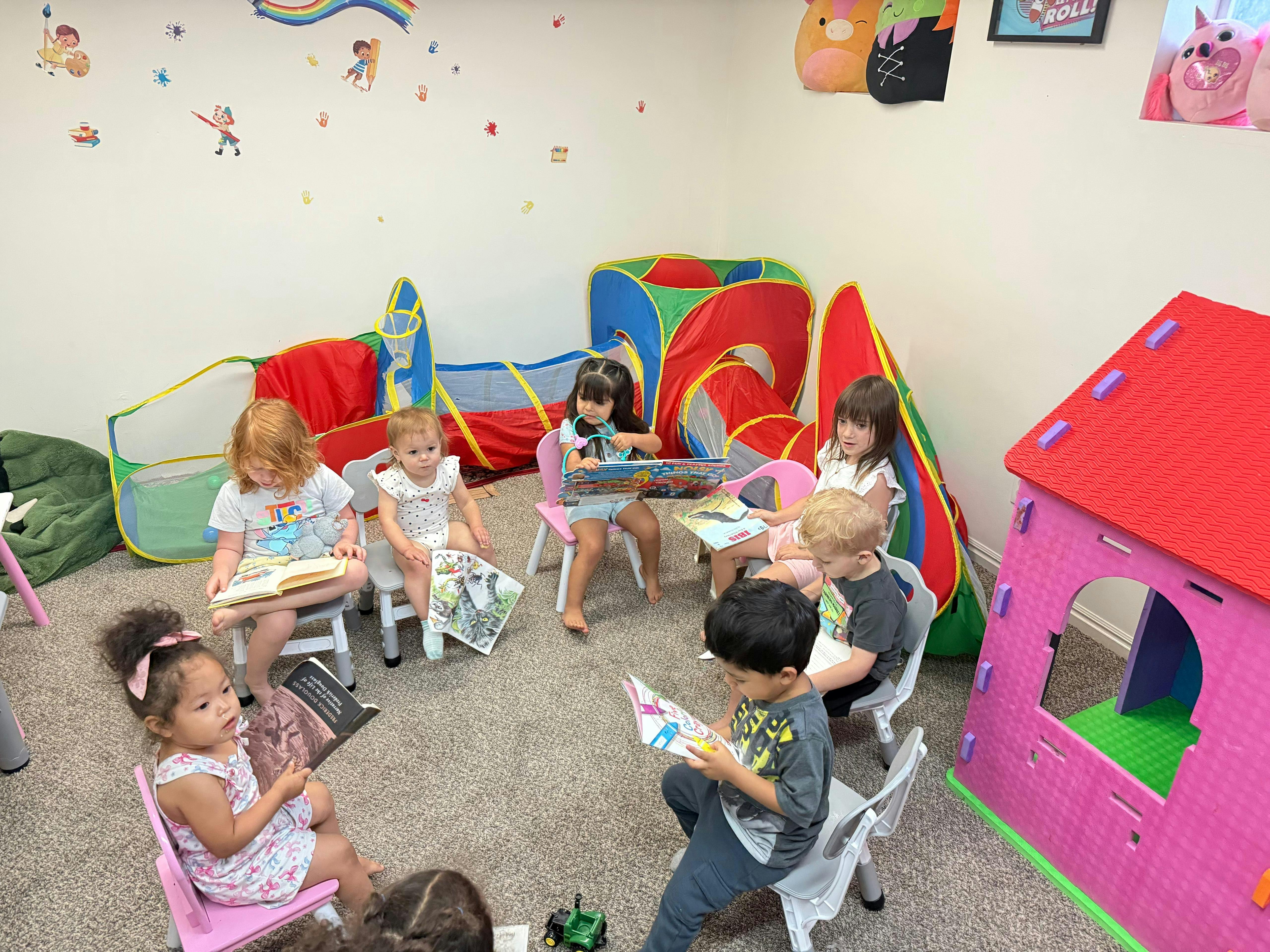 Group of children sitting on chairs in a circle reading books indoors