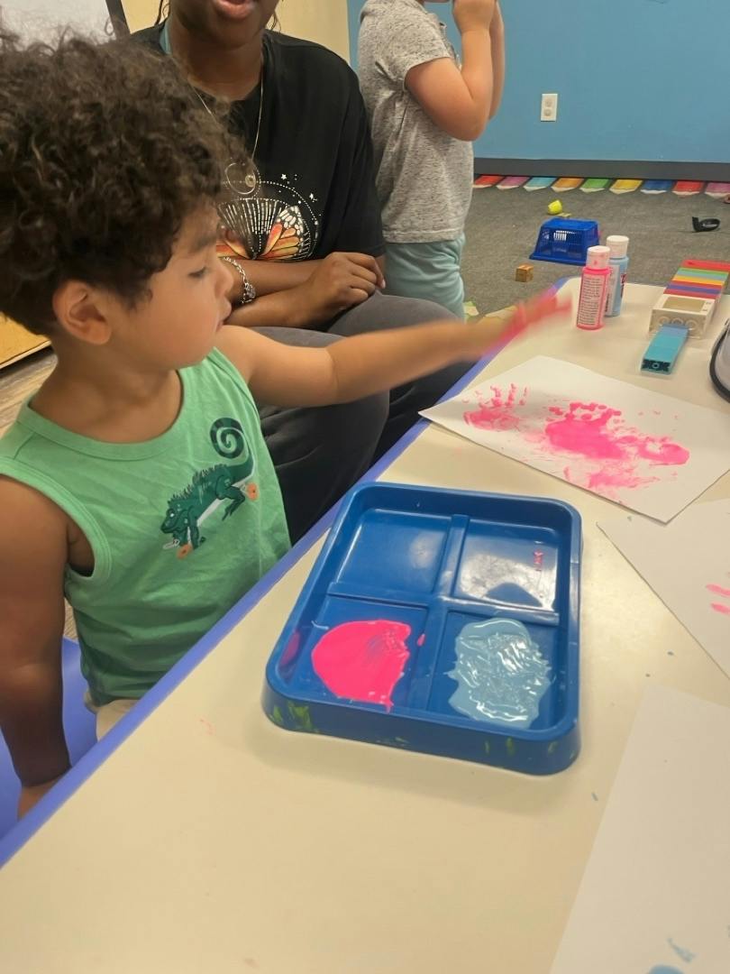 Child making handprints with pink paint at a table