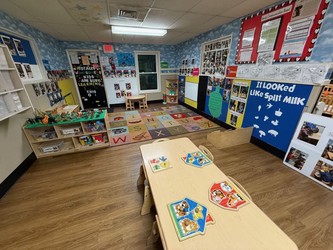 Classroom with a colorful alphabet rug, small tables, shelves of toys and books
