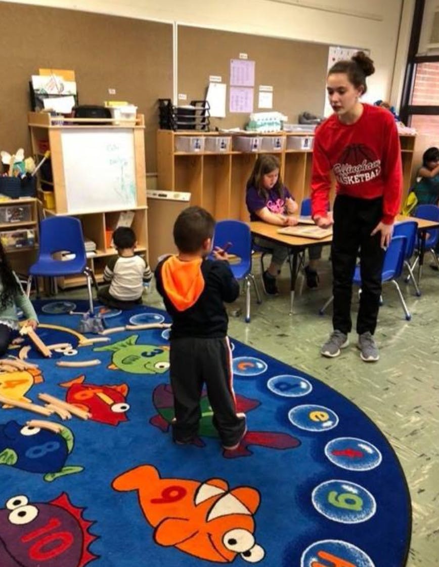 Teen and child standing on a colorful rug in a classroom