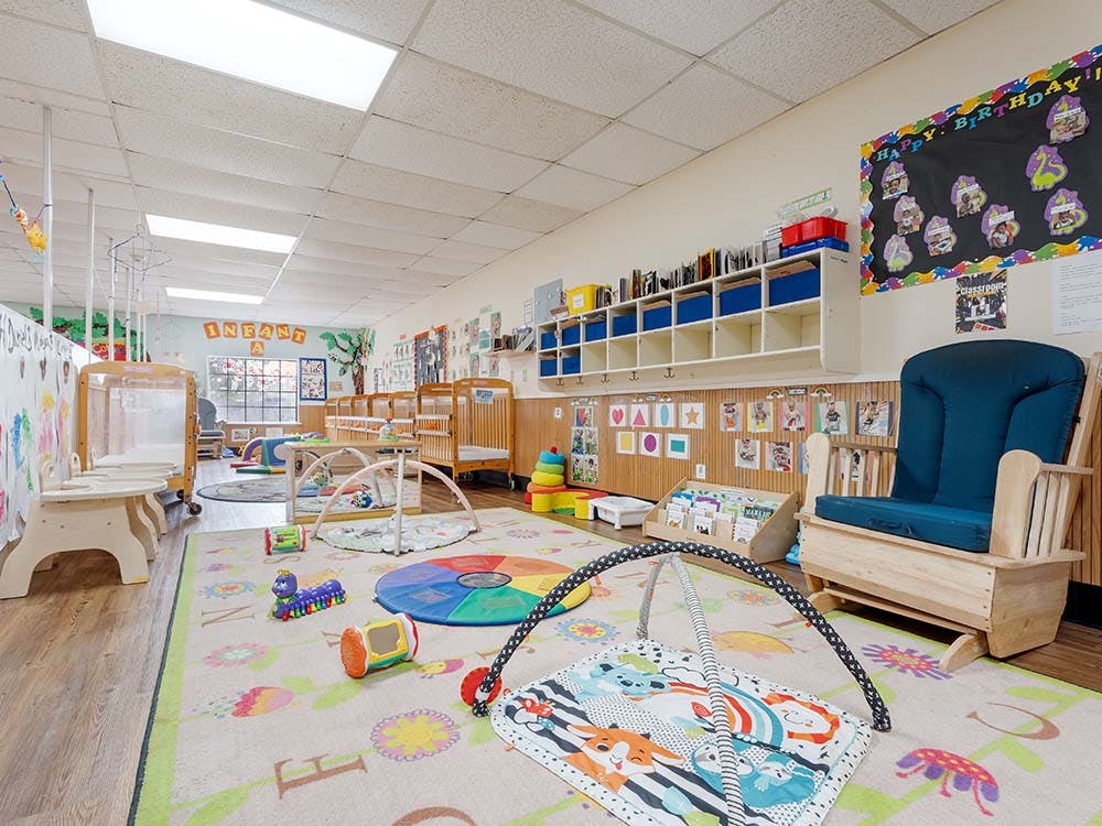 An infant daycare classroom with cribs, playmats, and a rocking chair