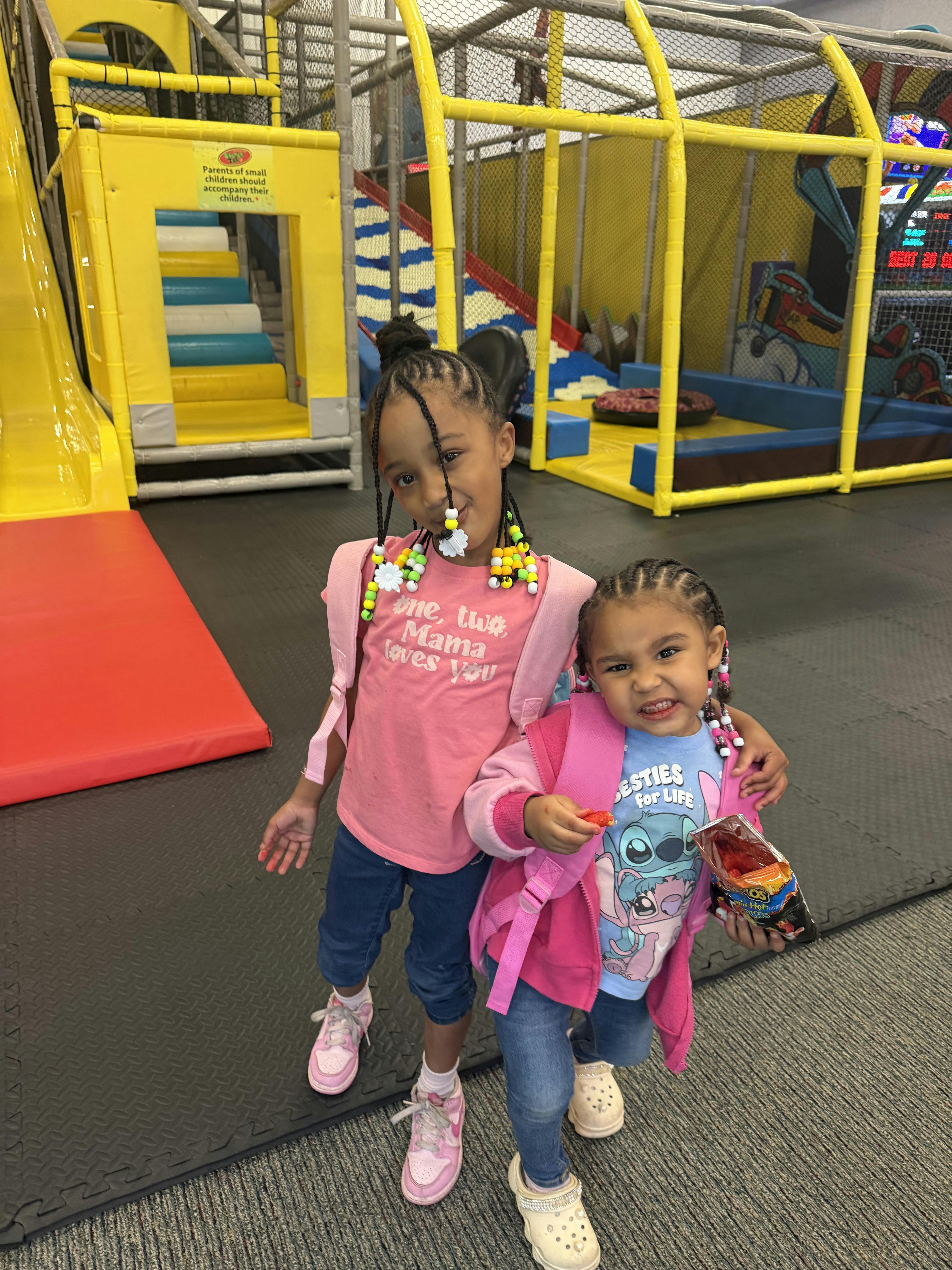 Two children wearing backpacks standing in an indoor playground