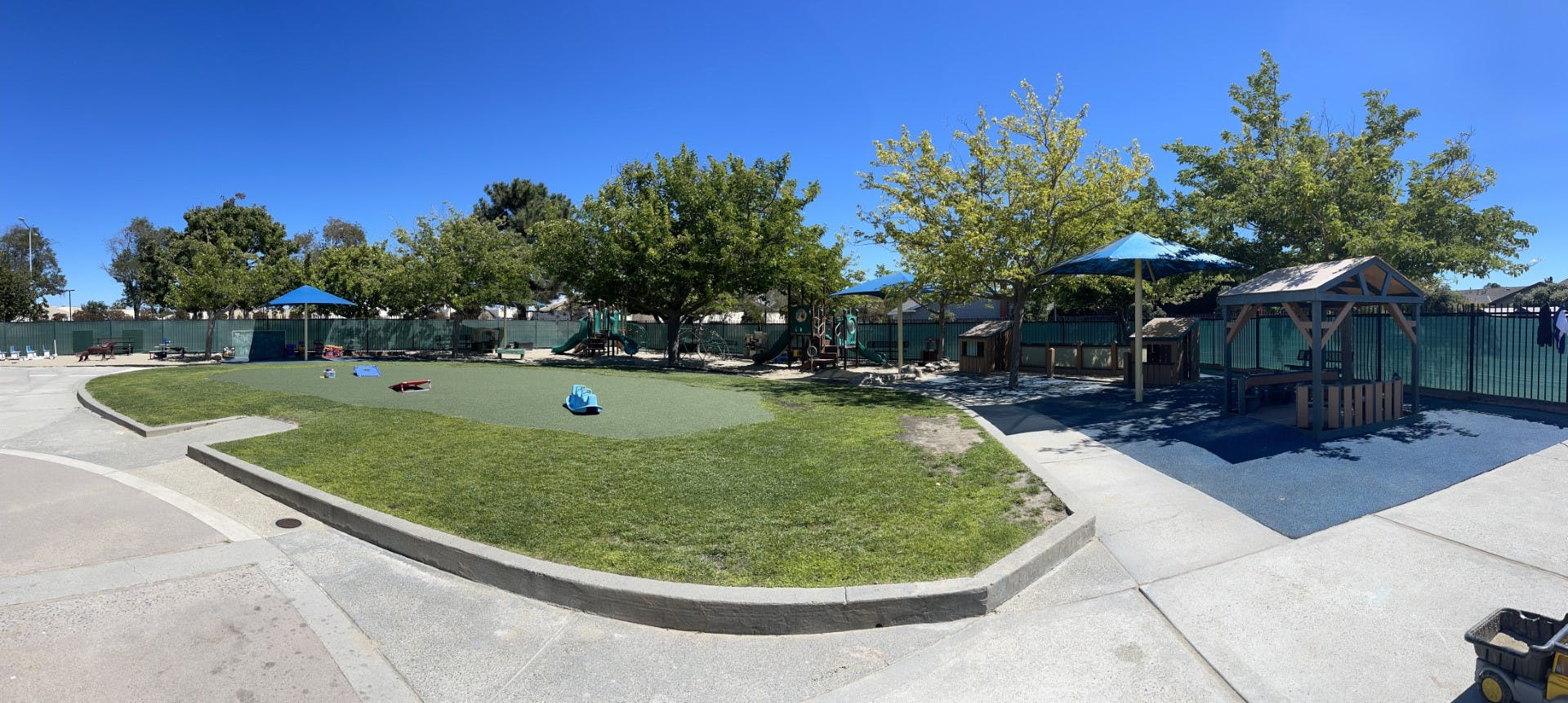 An empty outdoor children's playground with grass, play structures, and shaded areas
