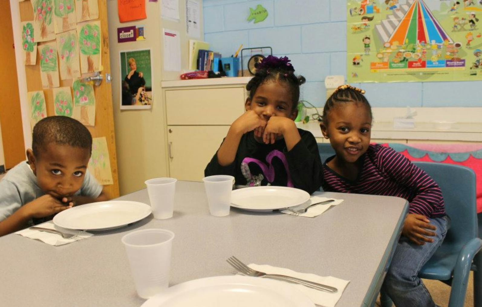 Three children sitting at a table with plates and cups