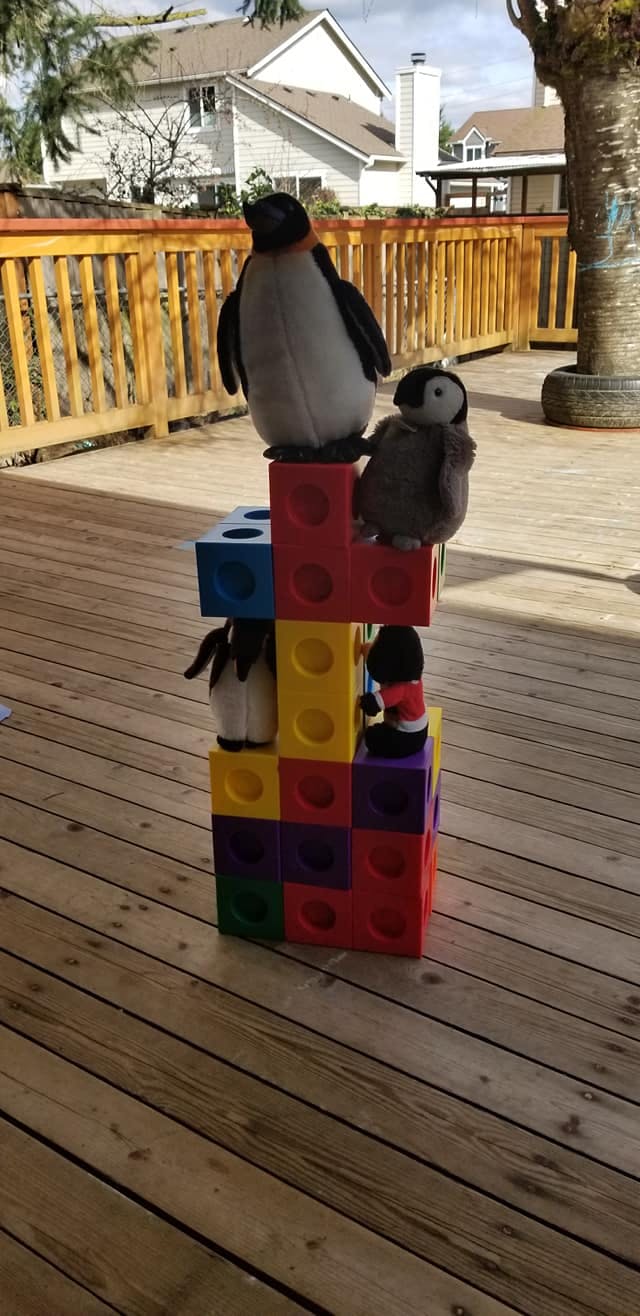 Penguin stuffed animals on colorful blocks on a wooden deck