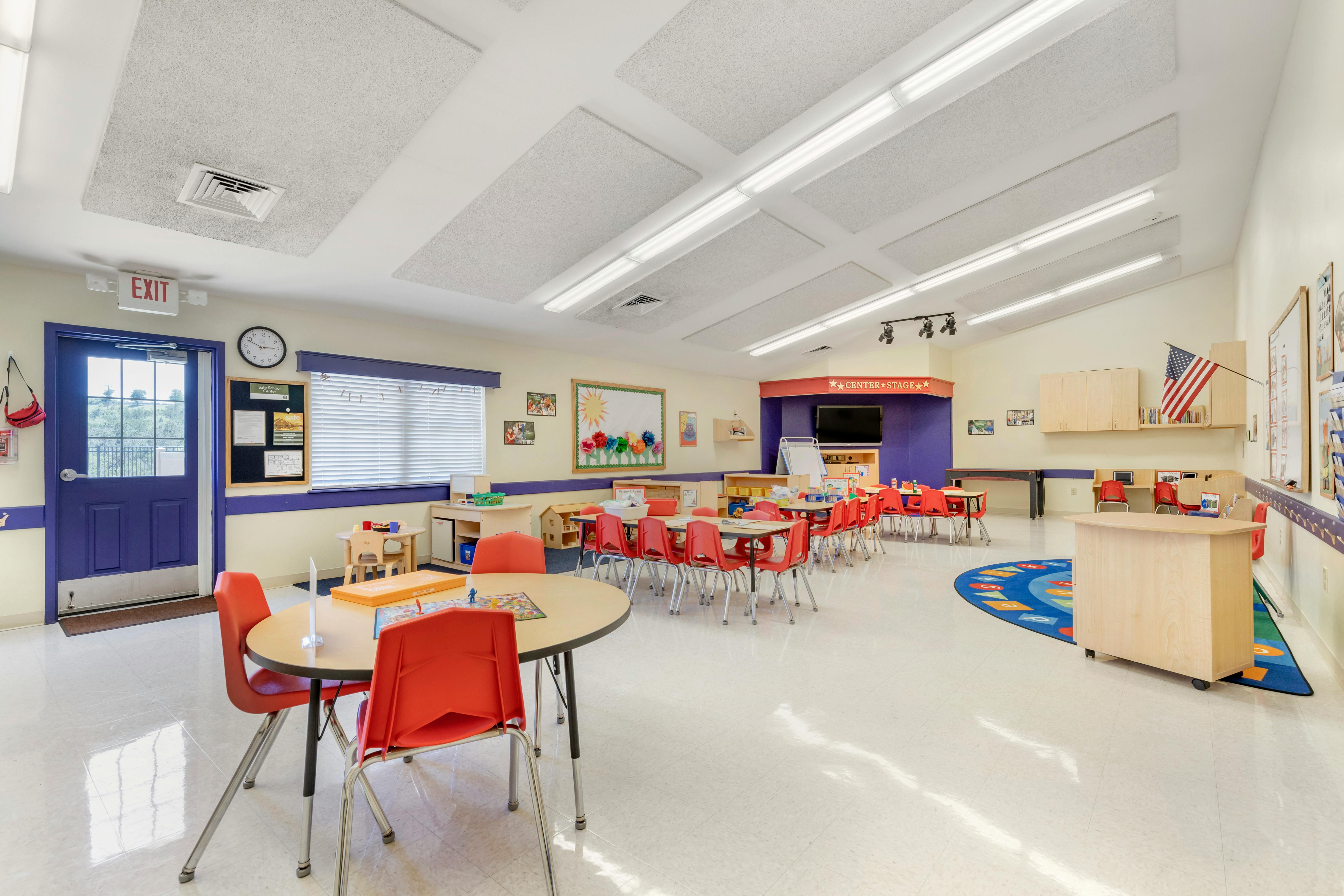 Classroom with small tables and red chairs, exit sign above door
