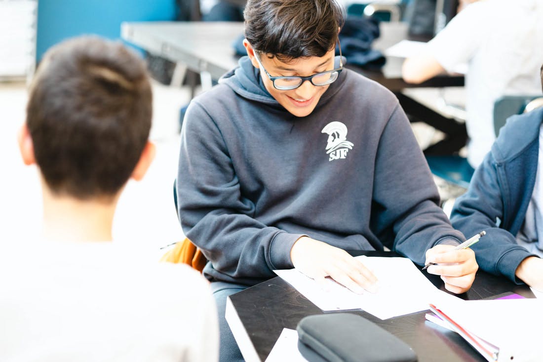 Teenager with glasses smiling while writing on a paper