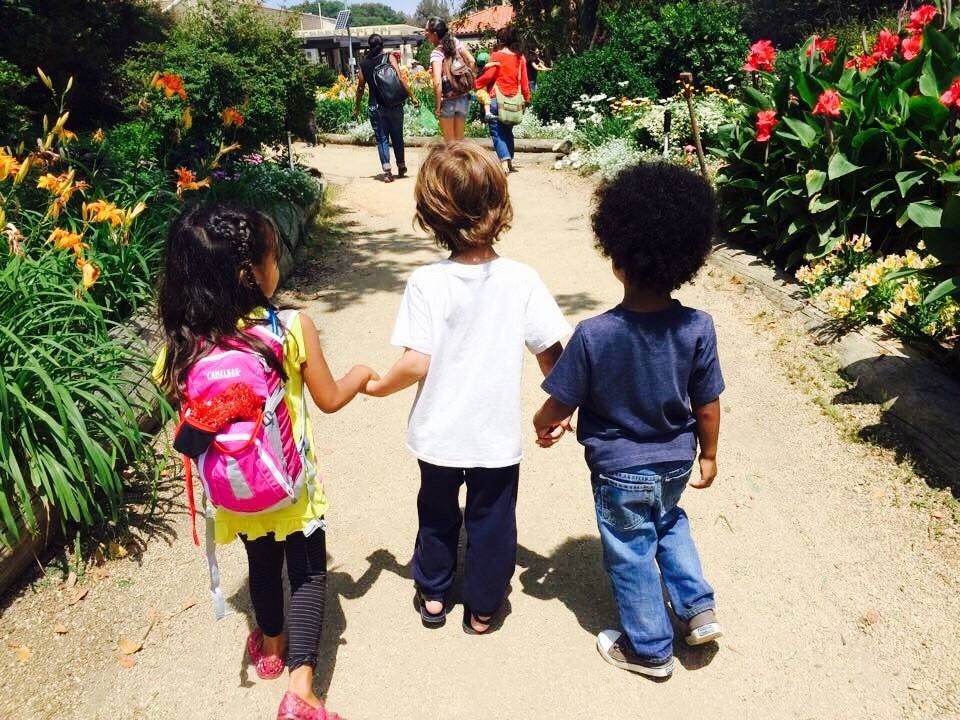 Three children holding hands walking on a path