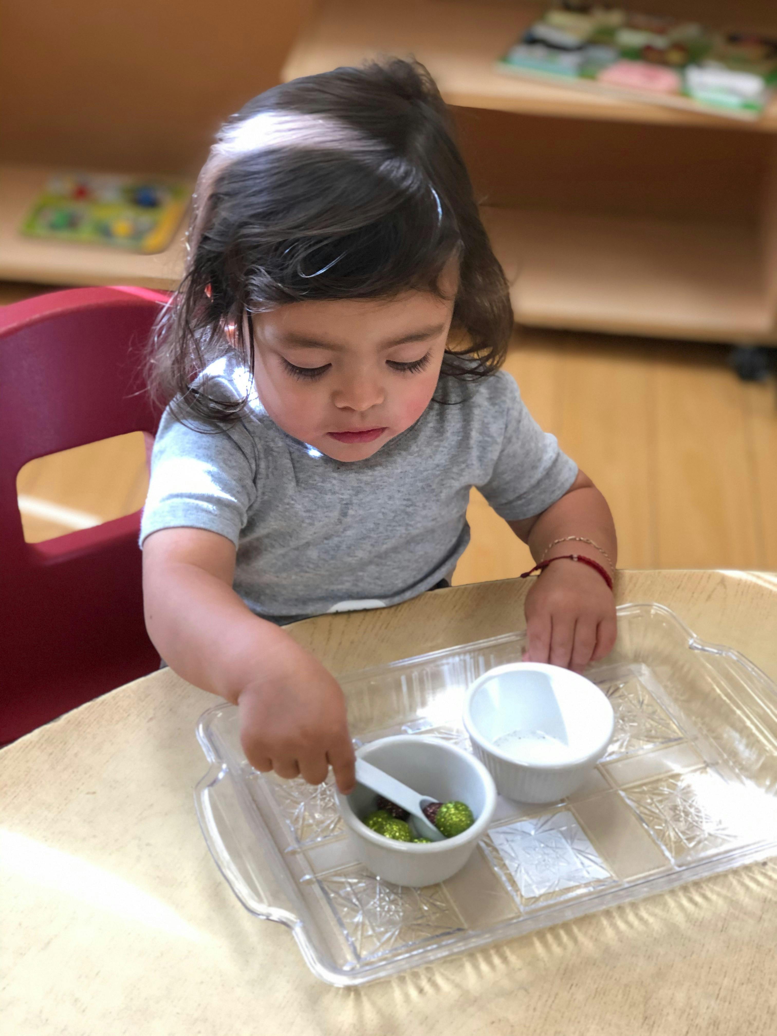 Child using a spoon to transfer items between small bowls