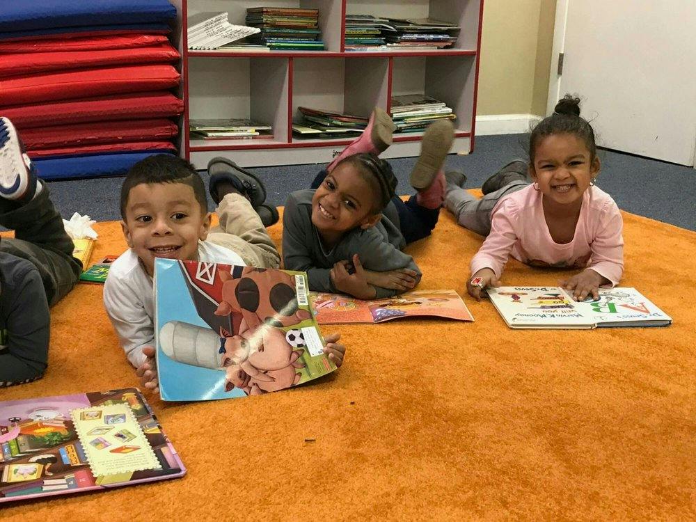 Three children lying on a rug with open books