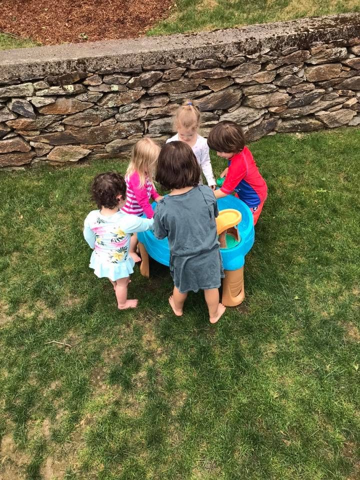 Five children playing around a water table outdoors