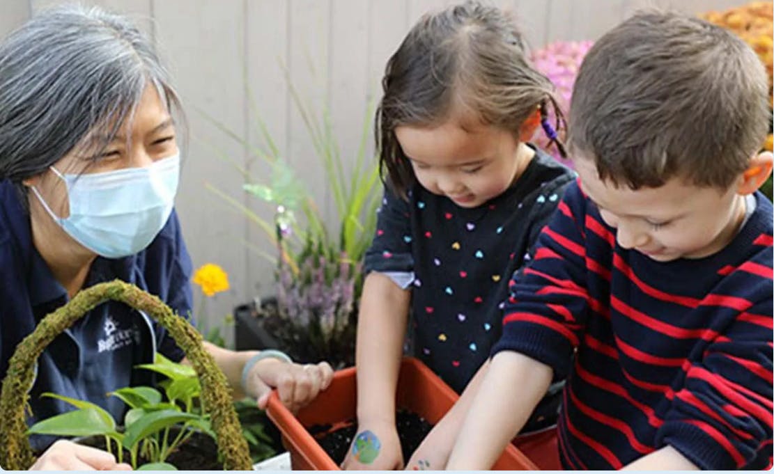 Person in mask with two children planting in a container