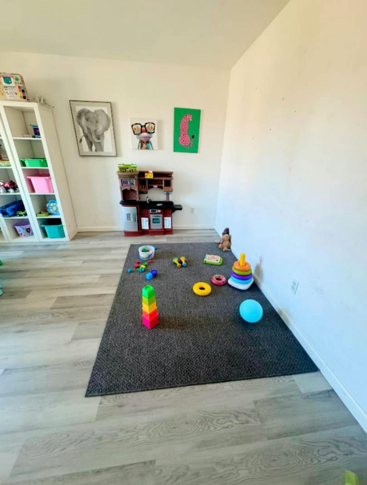 A playroom with a toy kitchen, bookshelf, rug, and various toys