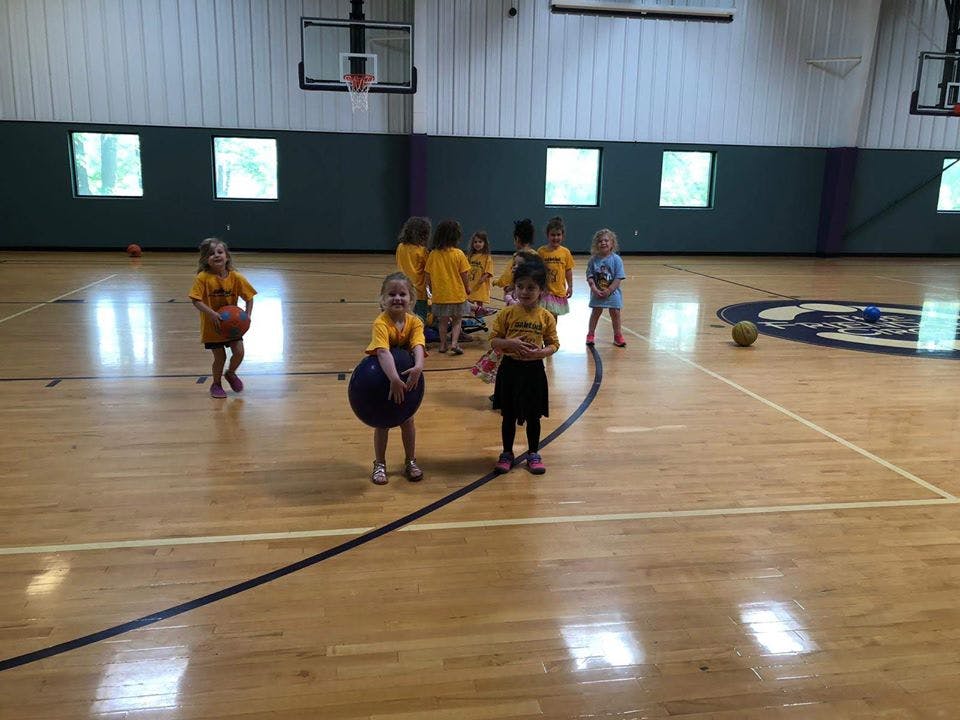 Children in yellow shirts playing with balls on a basketball court