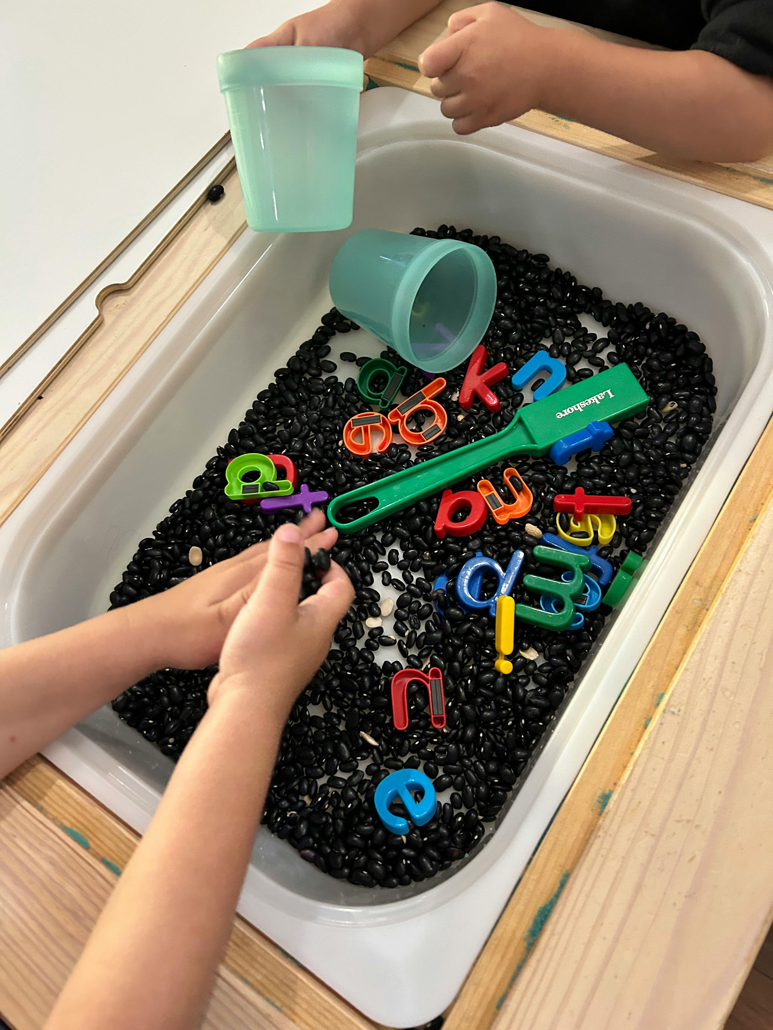 Child's hands playing with beans and alphabet letters in a sensory bin