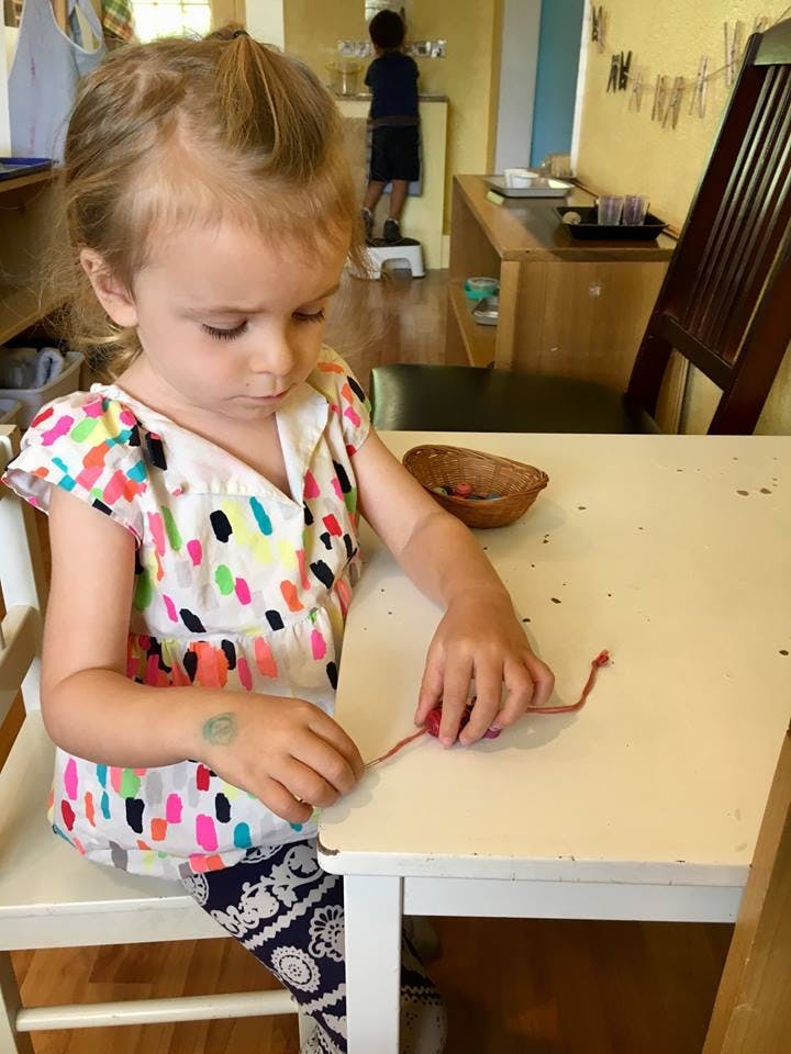Child sitting at a table, working with red yarn