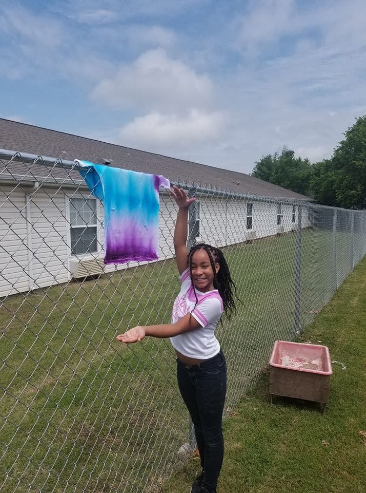 Teen standing next to a fence with a tie-dye shirt hanging on it