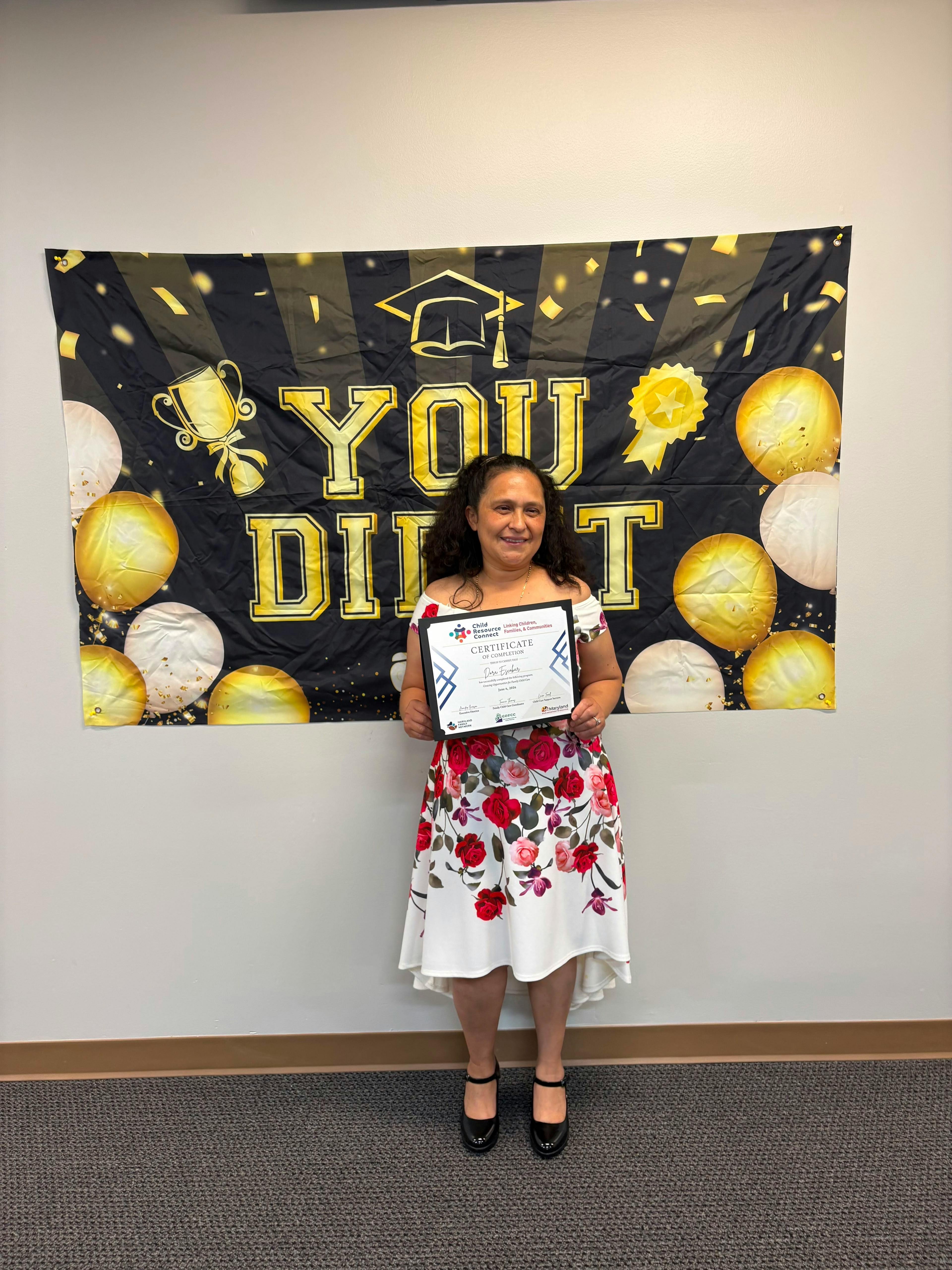 Person holding a certificate in front of a banner that says "YOU DID IT"