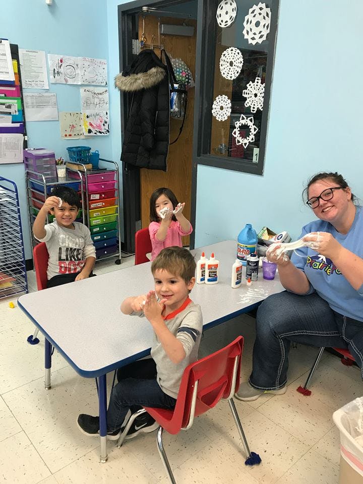 Adult and three children at a table making crafts in a classroom