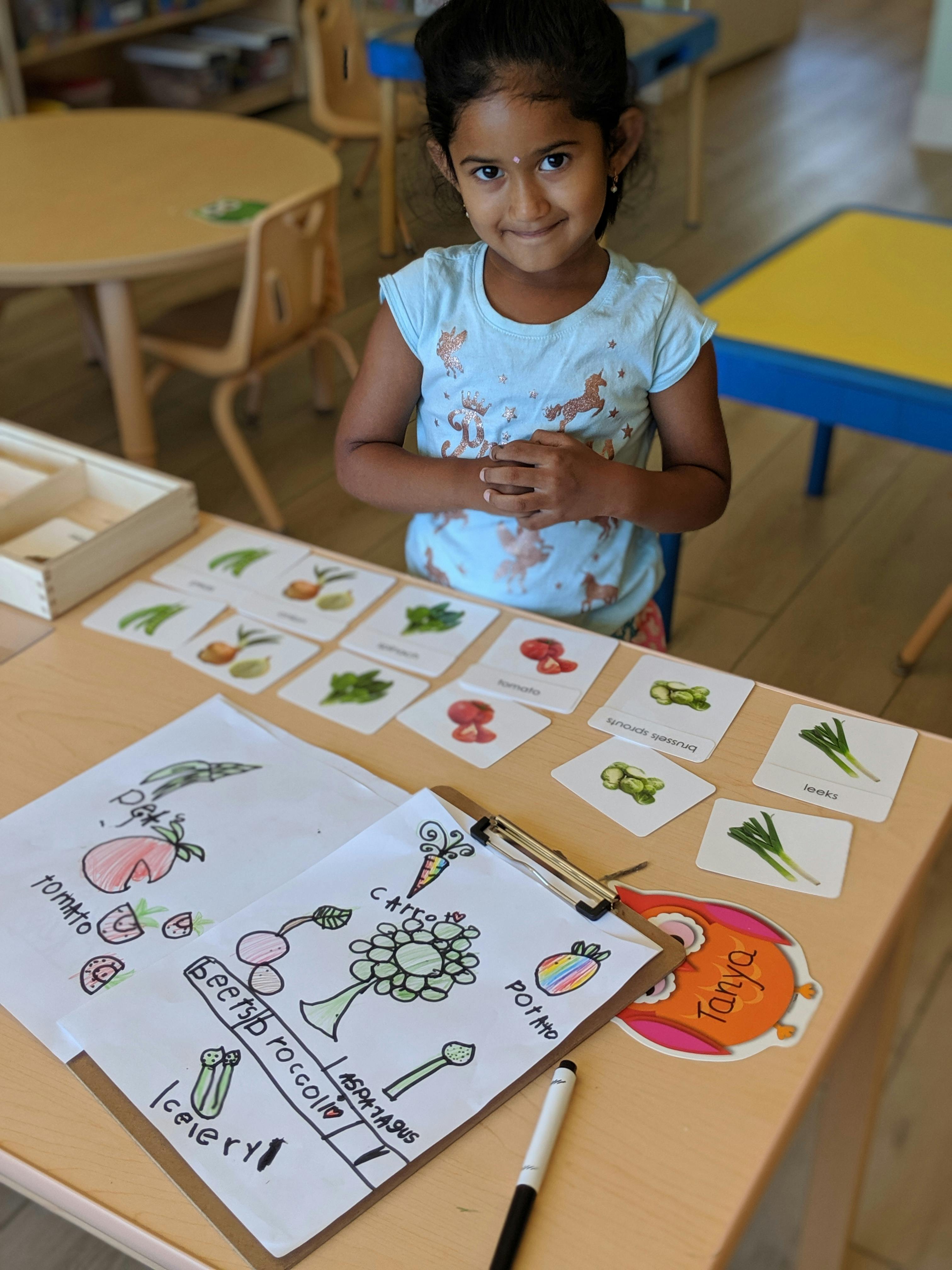 Child standing at a table with vegetable flashcards and drawings