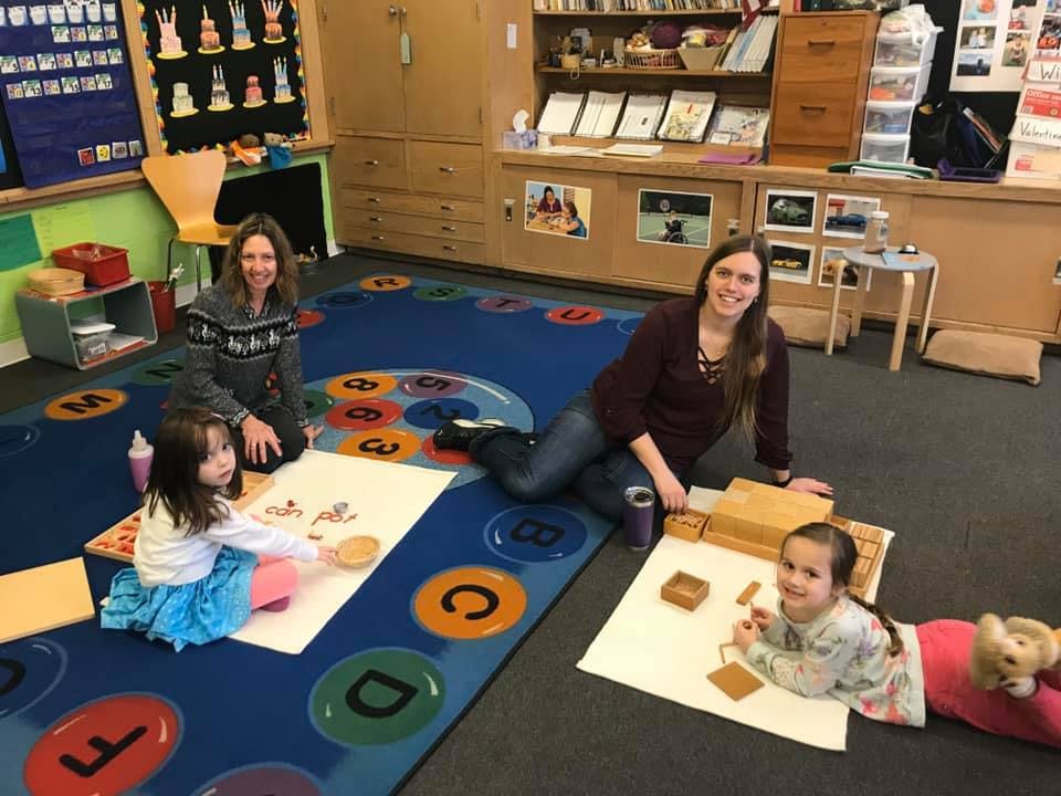 Two adults and two children on the floor in a classroom