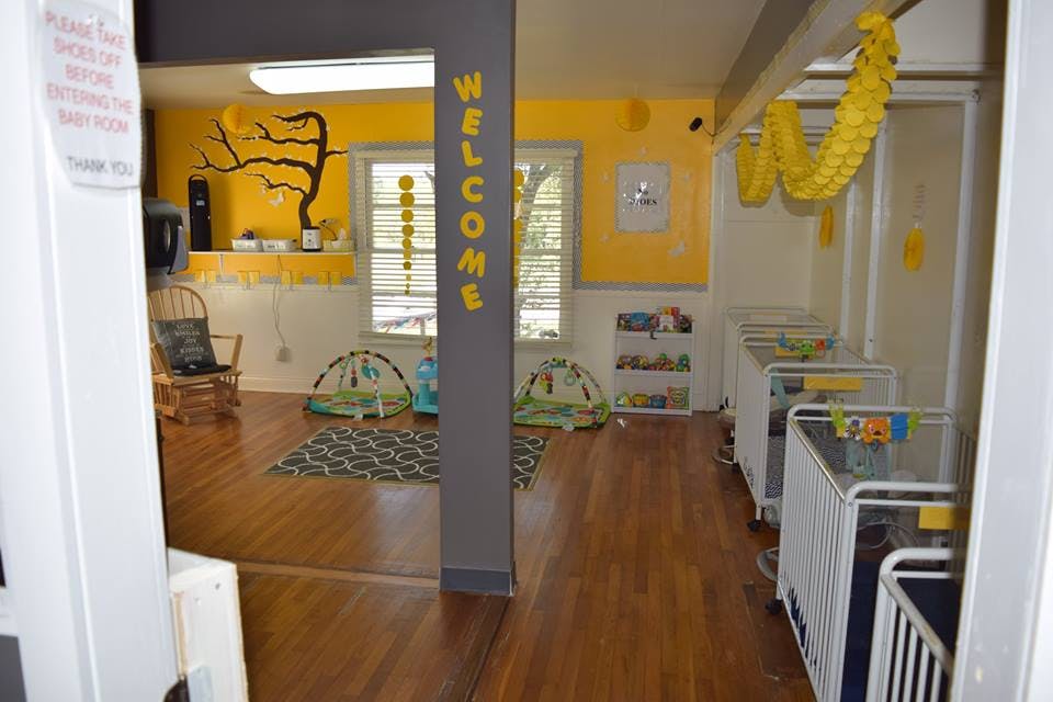 Nursery room with cribs and play mats, yellow walls, and a welcome sign