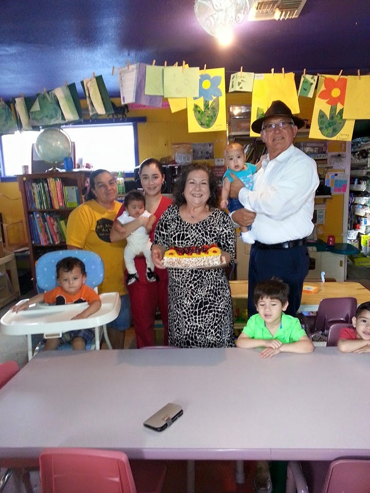 Group of people and children in a classroom, one person holding a cake