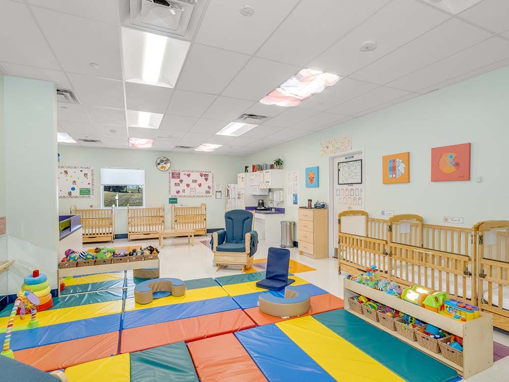 A colorful daycare room with play mats, cribs, and toys