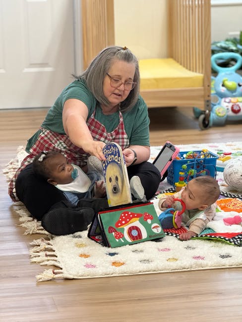 Person reading a book to two children on a rug