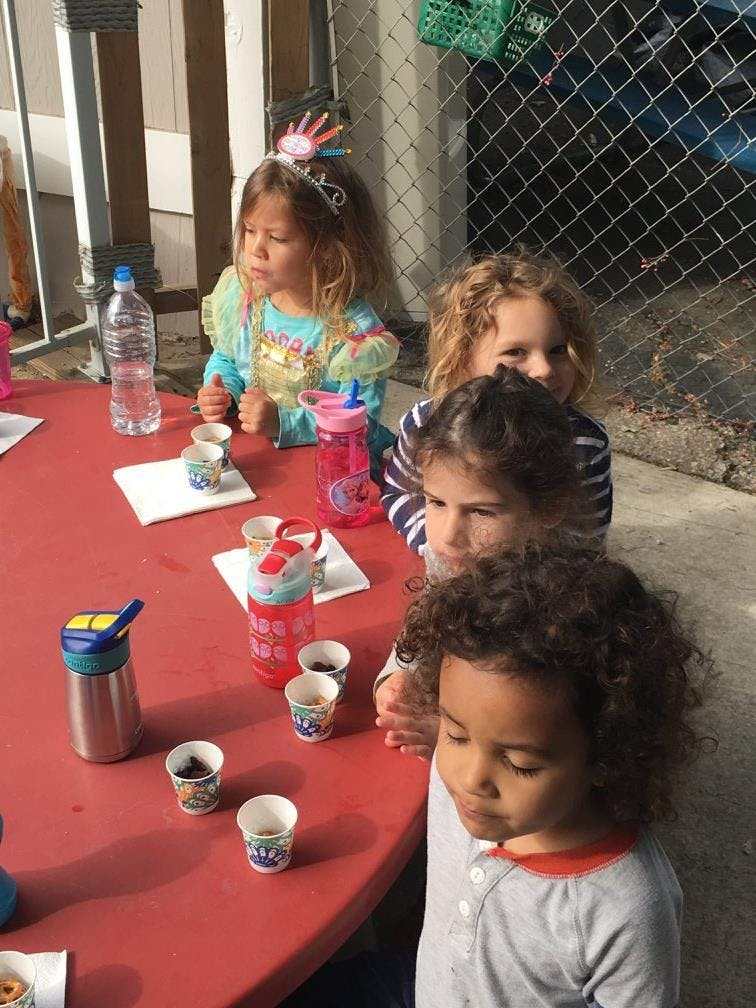 Four children sitting at a red table with small cups and water bottles