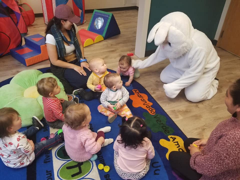 Person in bunny costume interacting with children and adults on a rug