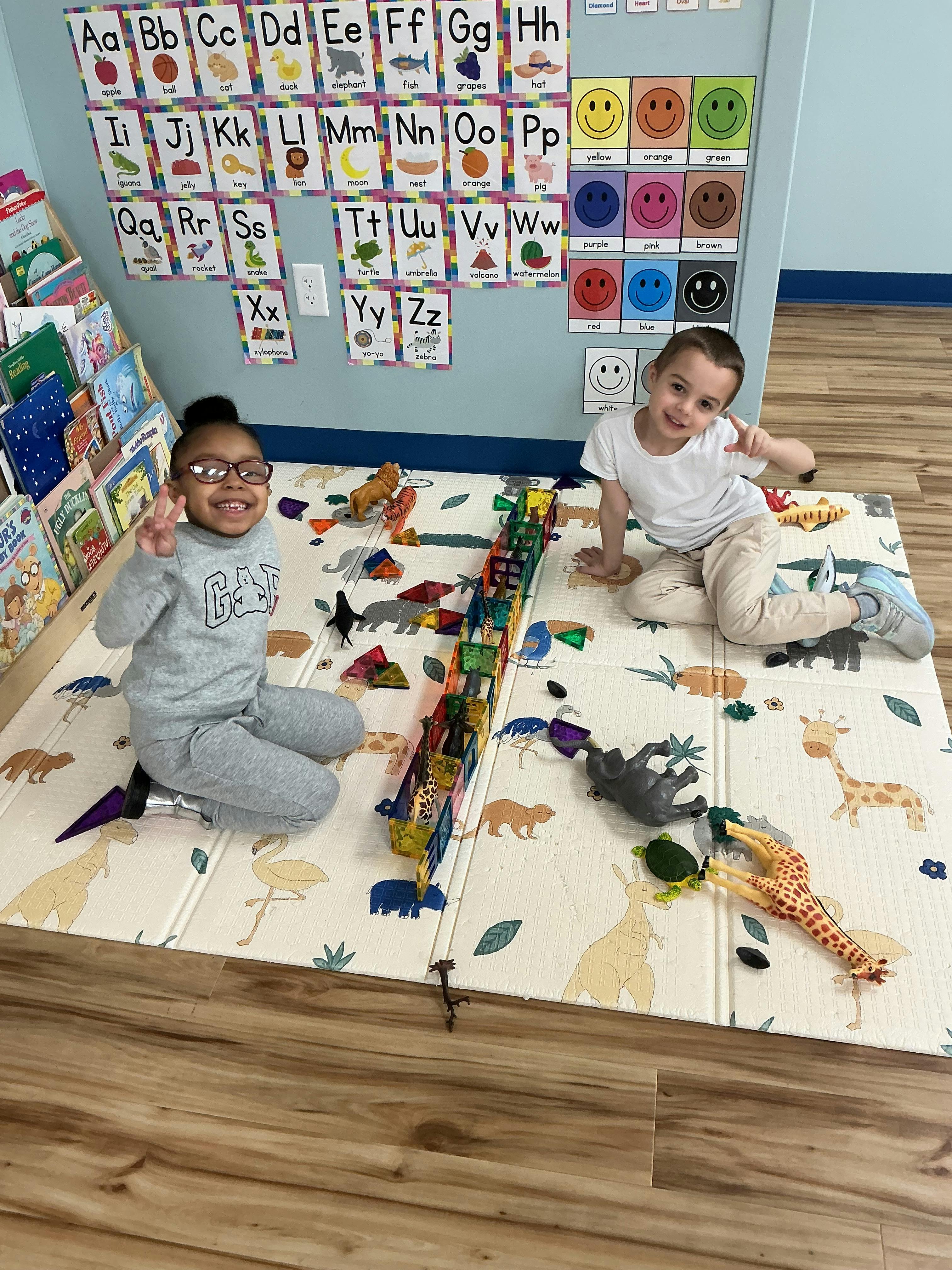 Two children playing on a mat with toys in the foreground shelves with books