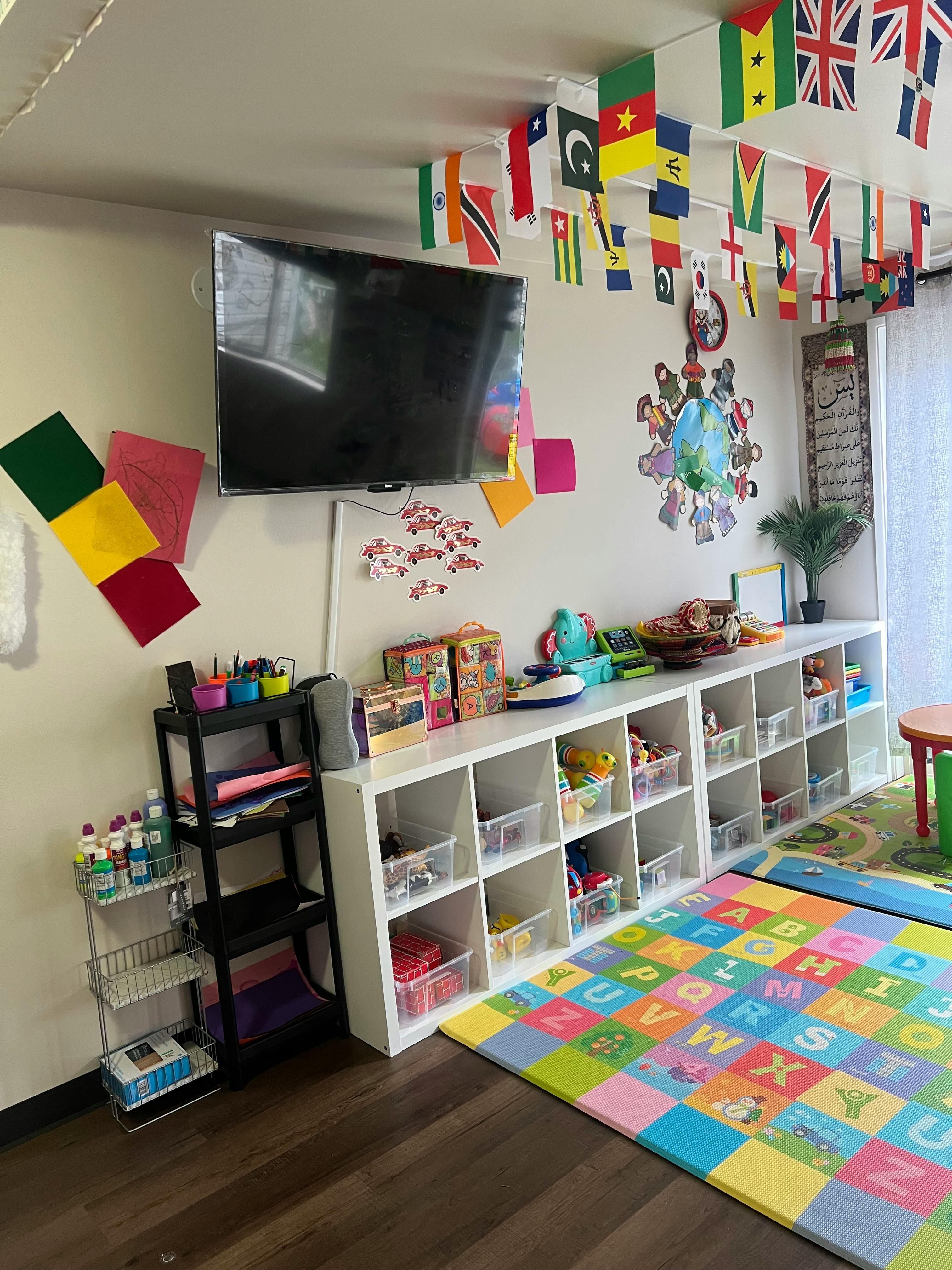 Playroom with a TV, shelves of toys, and a colorful alphabet mat