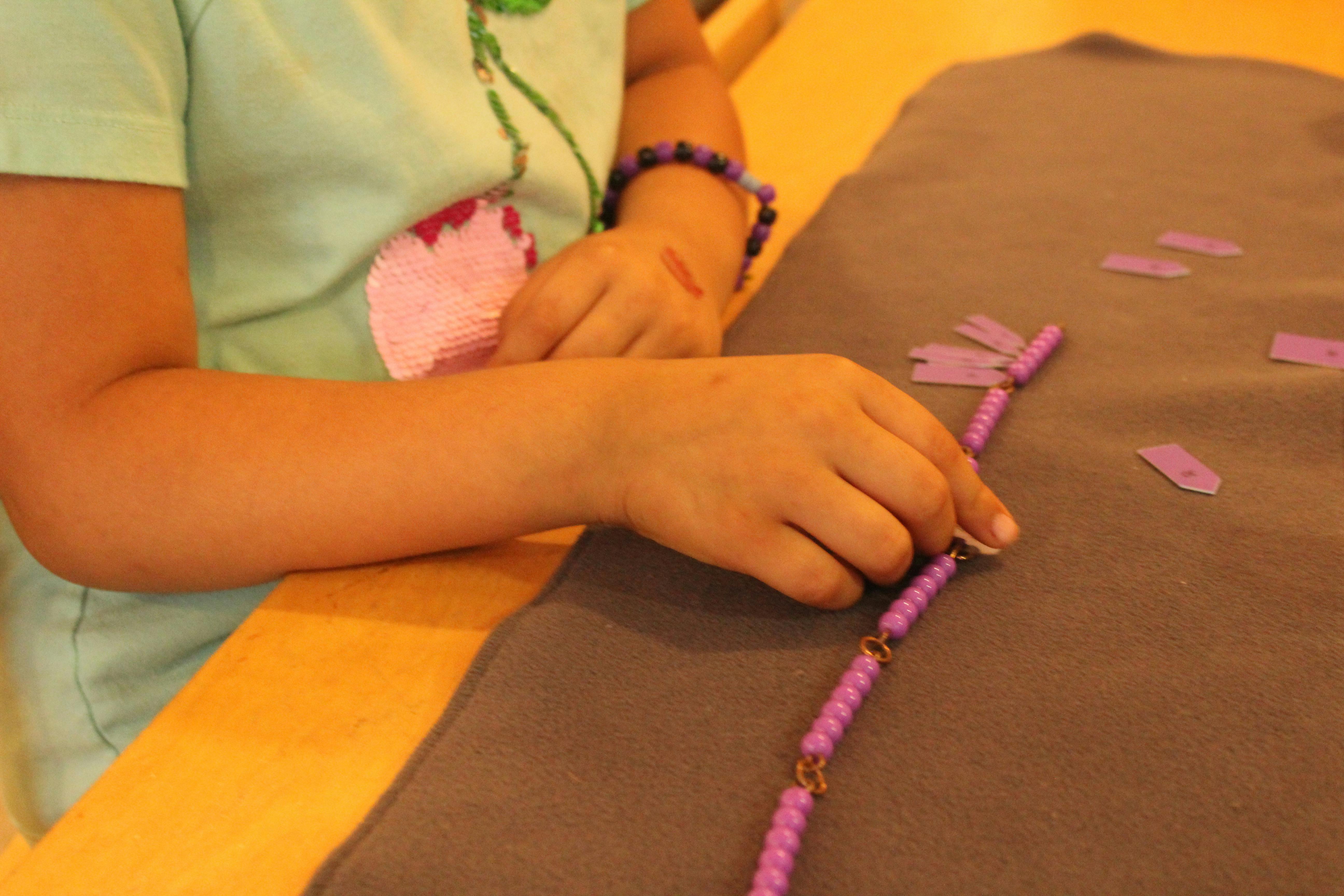 Child's hands working with purple beads on a brown surface