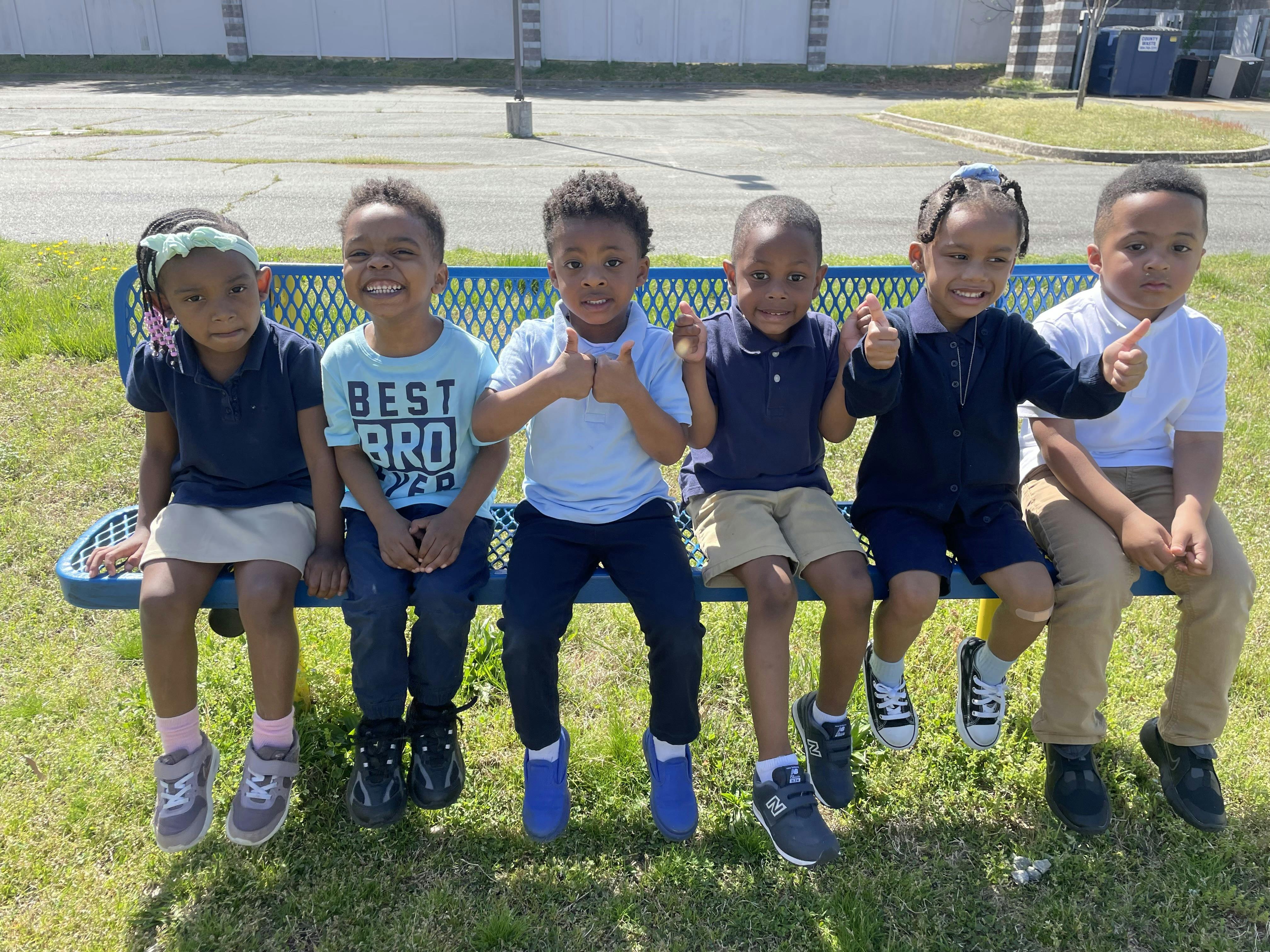 Group of six children sitting on a blue bench outdoors