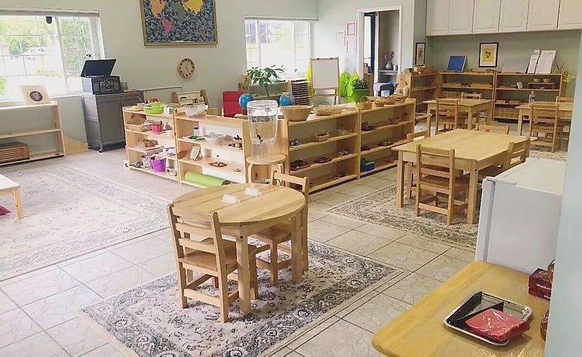Classroom with small wooden tables and chairs, shelves with learning materials
