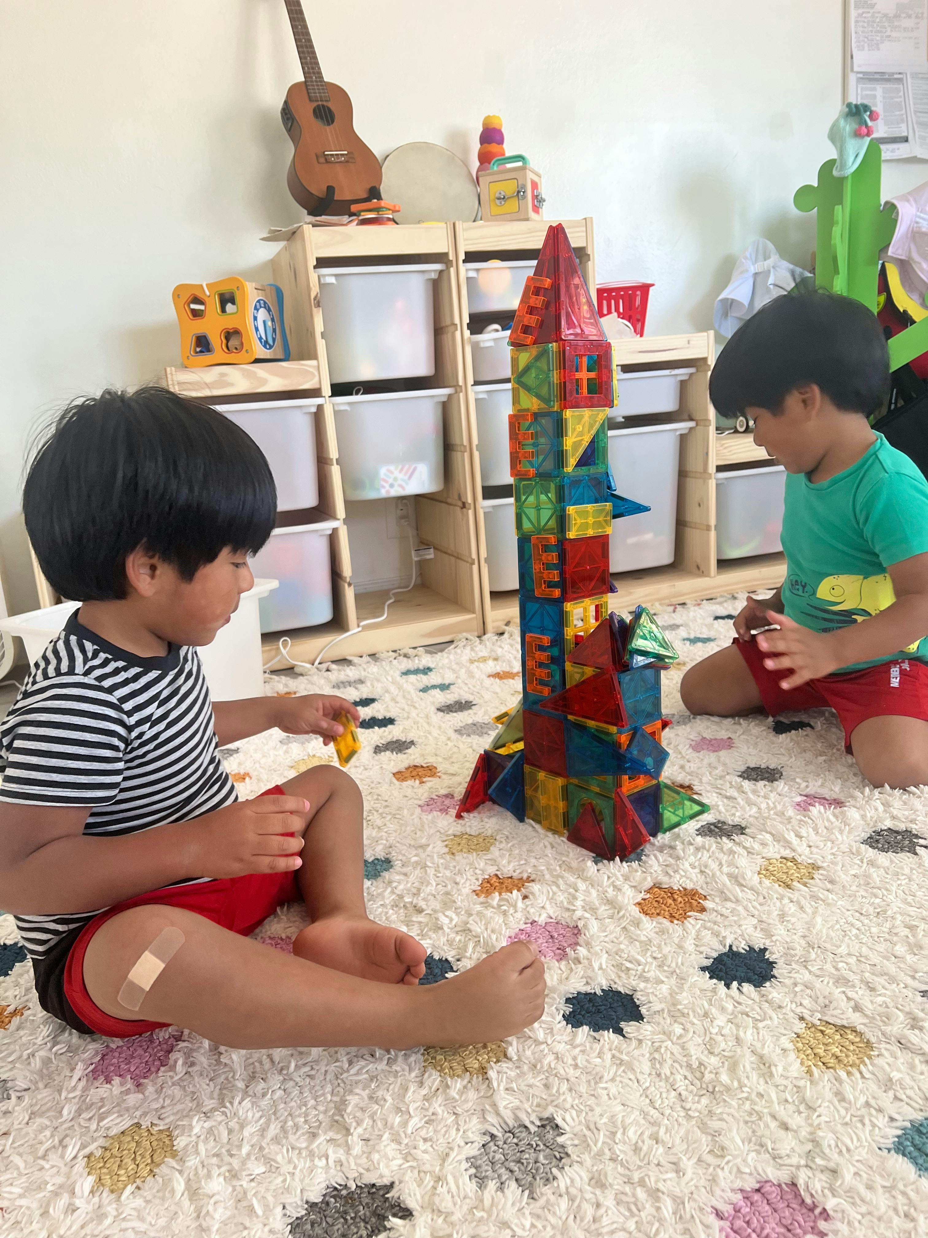 Two children playing with magnetic building blocks on a rug