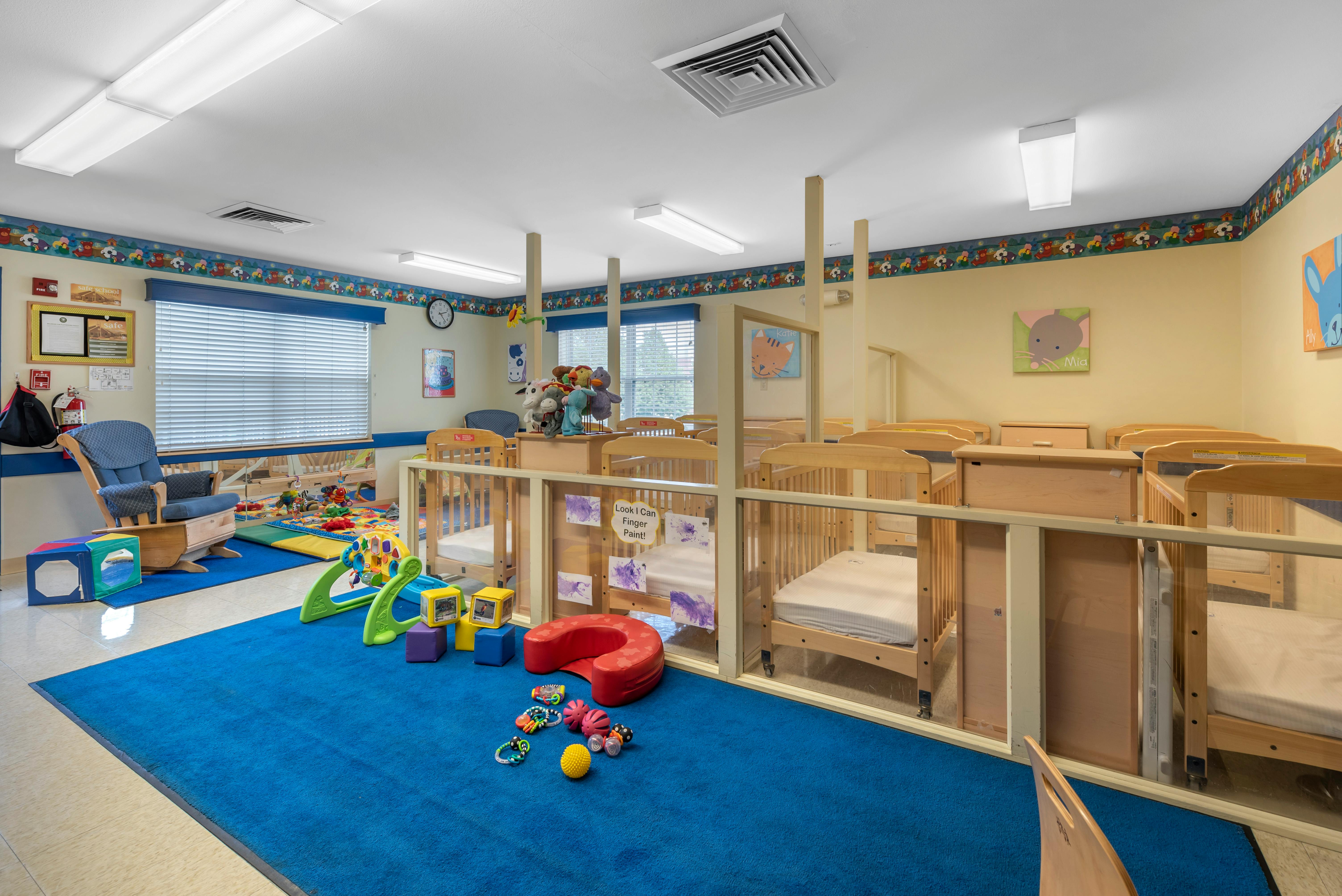 A daycare room with several cribs separated by glass partitions and a play area