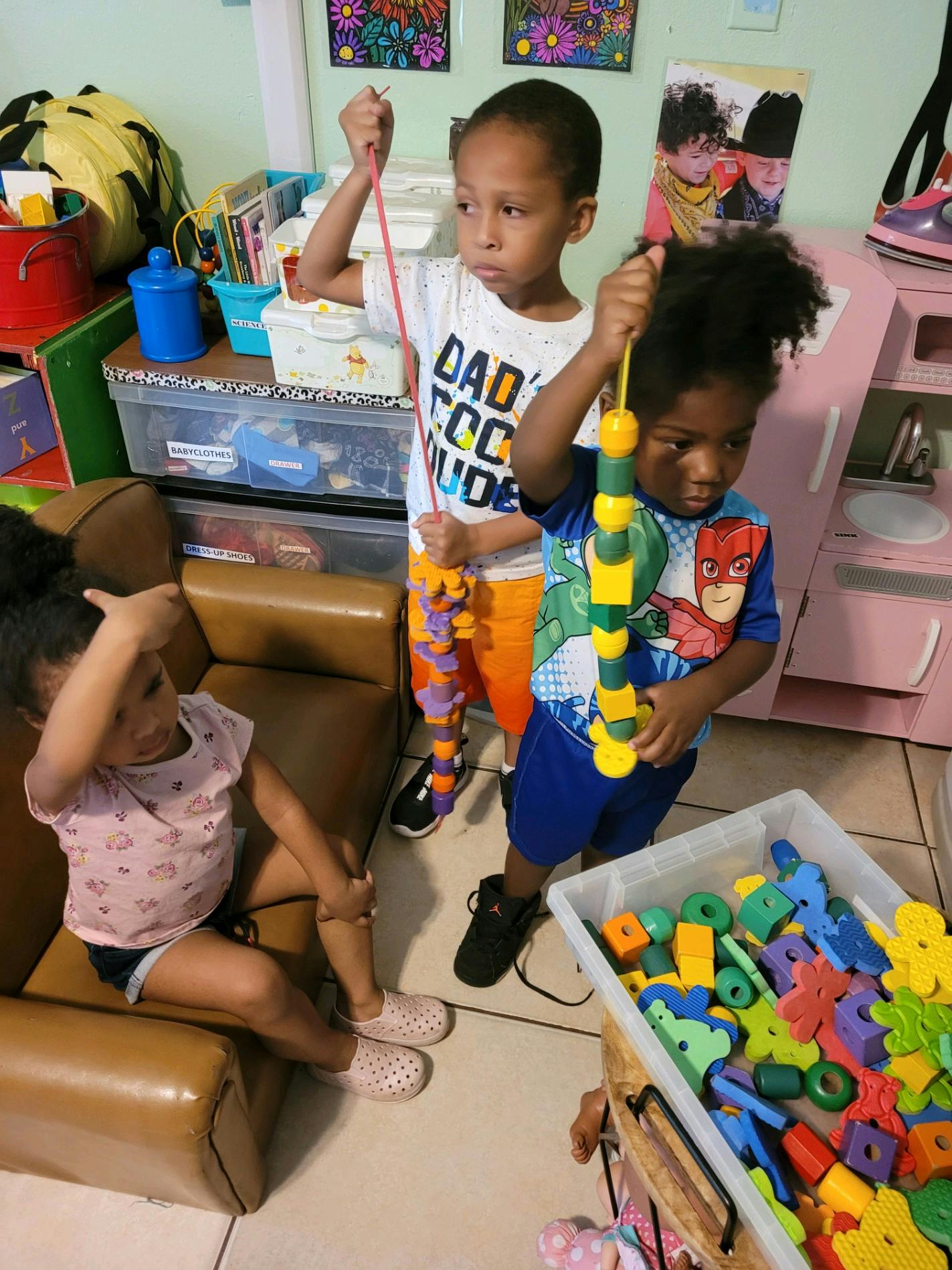 Two children holding up stringed toys, one child sitting on a chair